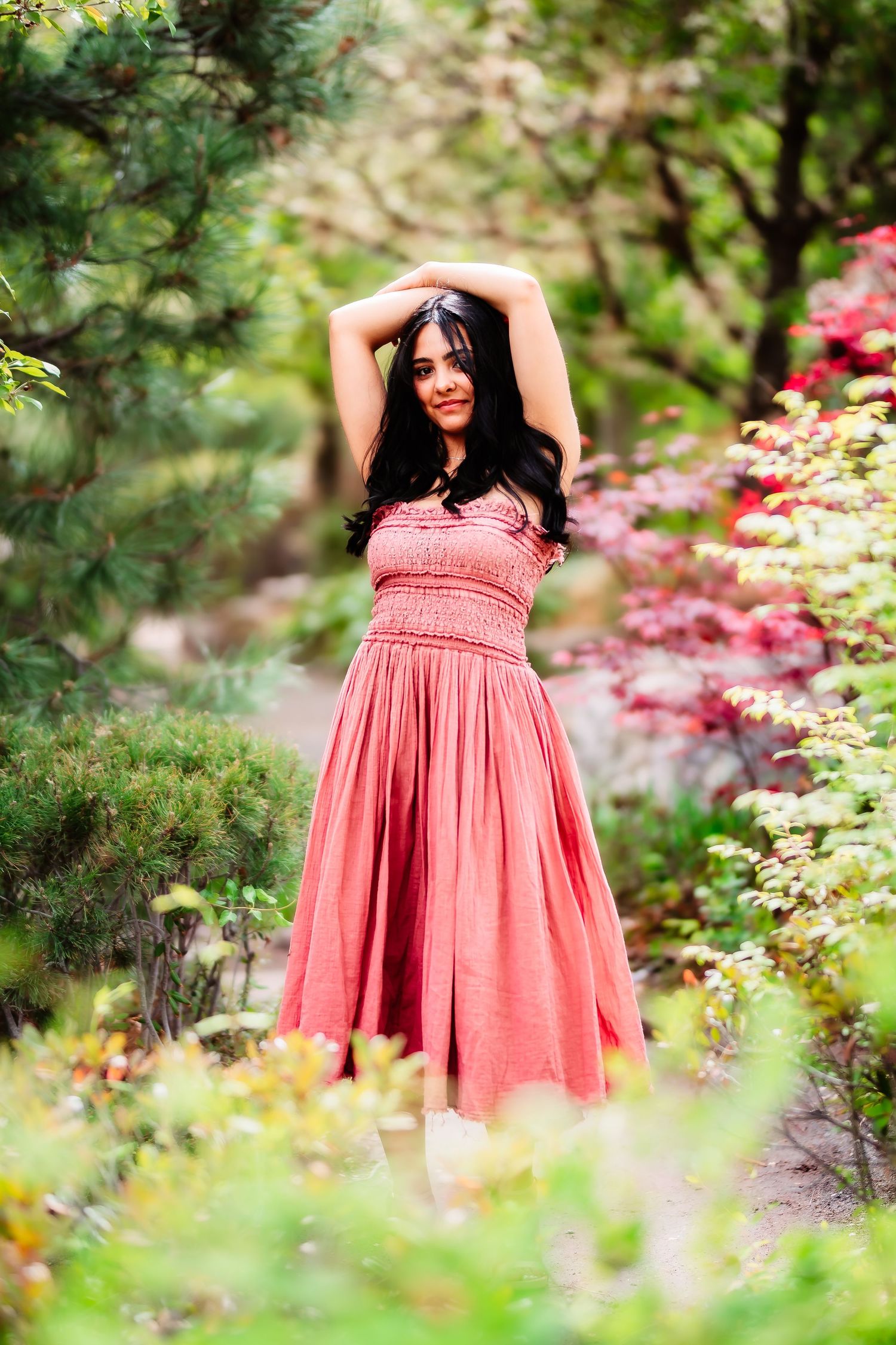A flowing coral dress twirls gracefully amidst colorful garden flowers and foliage.