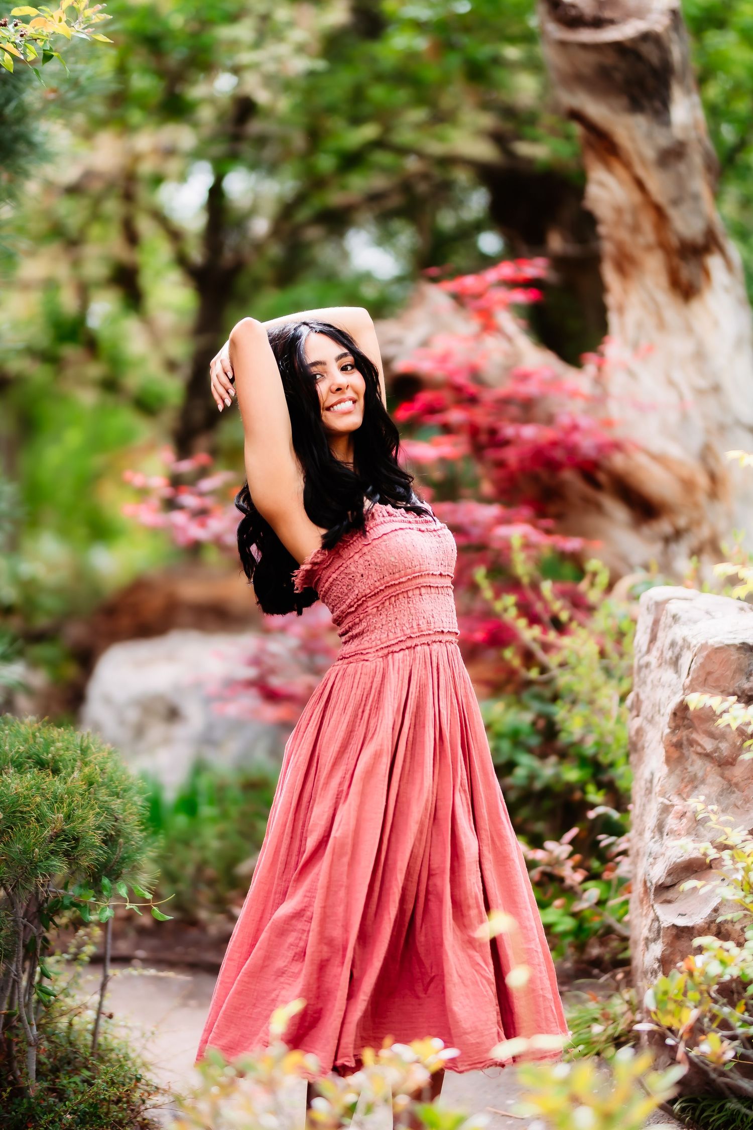 Elegant pose in a coral dress against vibrant red maple leaves and garden stones.