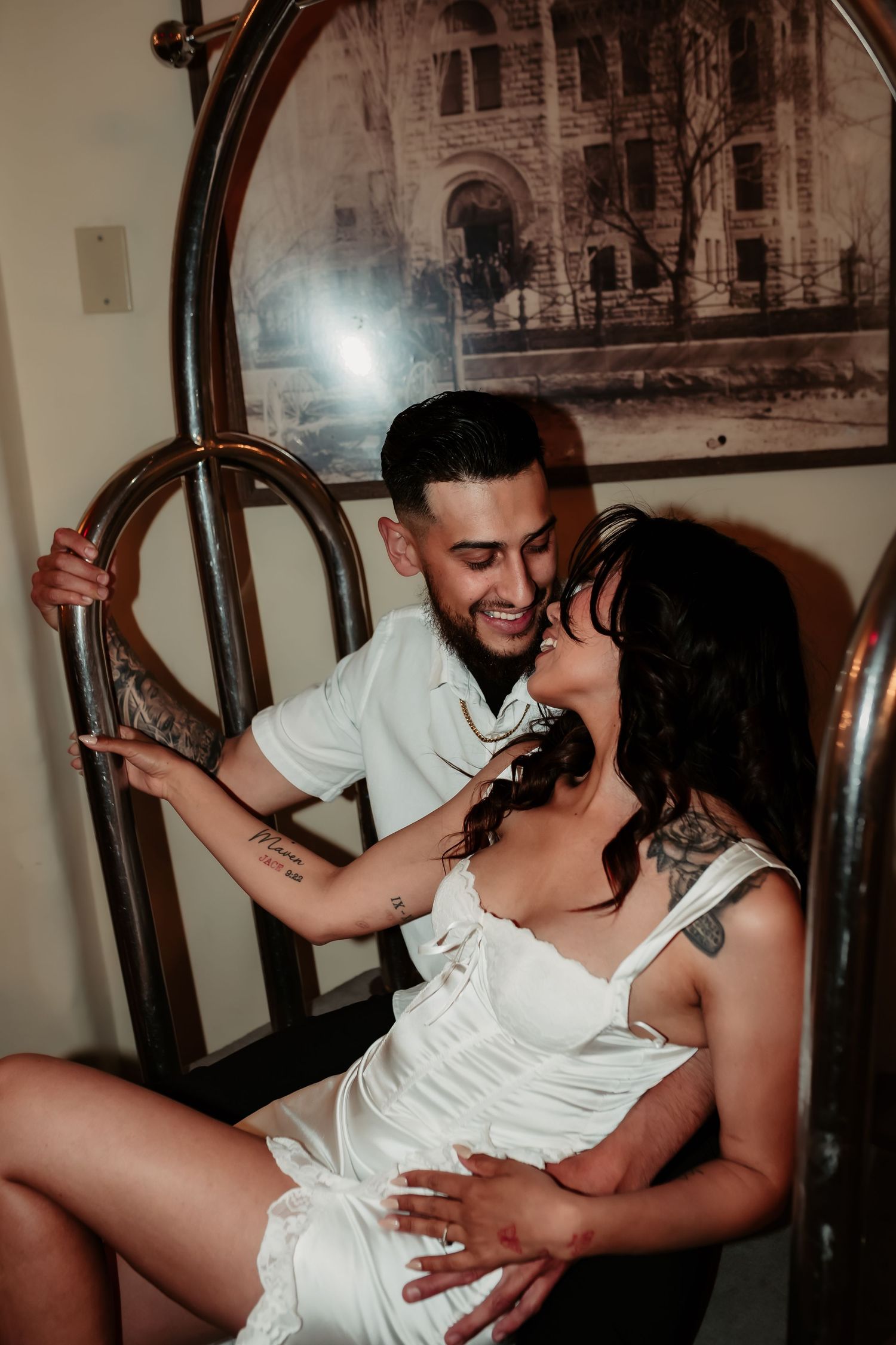 A romantic couple shares an intimate moment on a vintage luggage cart with classic architecture artwork in the background.