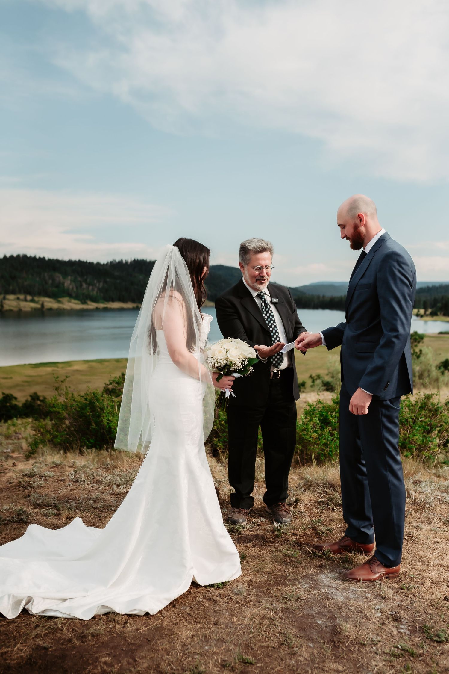 Wedding ceremony taking place on a hilltop overlooking a scenic lake.