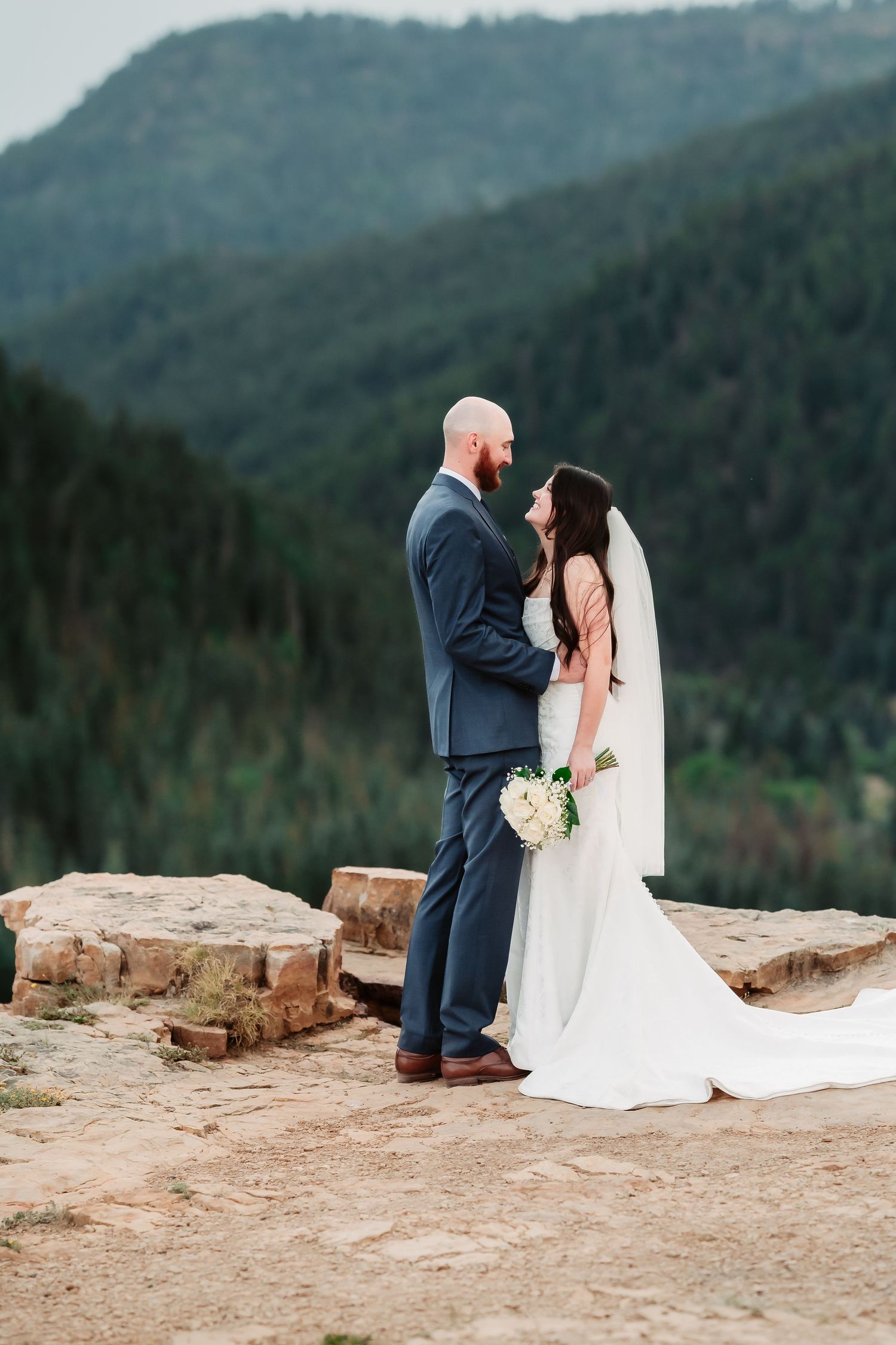 A romantic wedding portrait on a rocky mountain overlook with sweeping valley views.