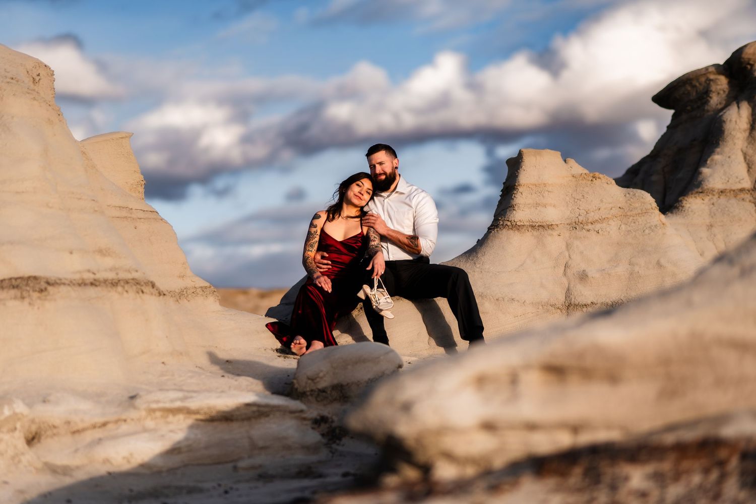Couple in formal wear sitting on dramatic white rock formations under cloudy sky.