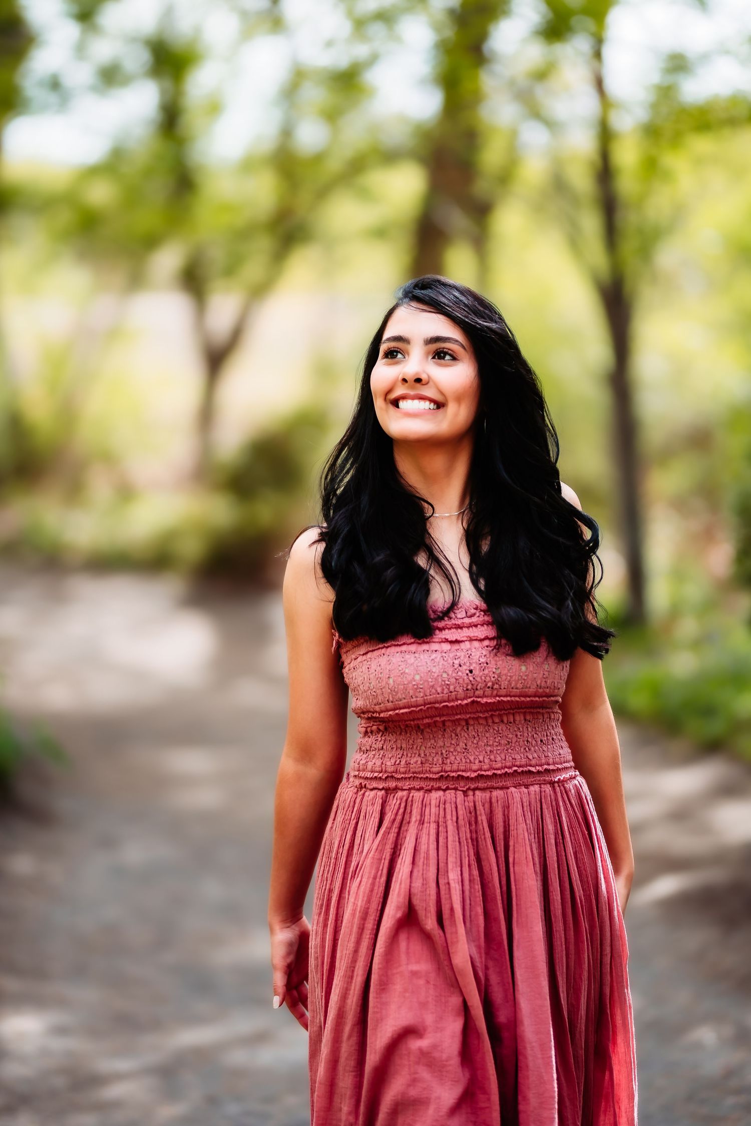 A person in a red maxi dress poses on a nature path surrounded by trees and greenery.