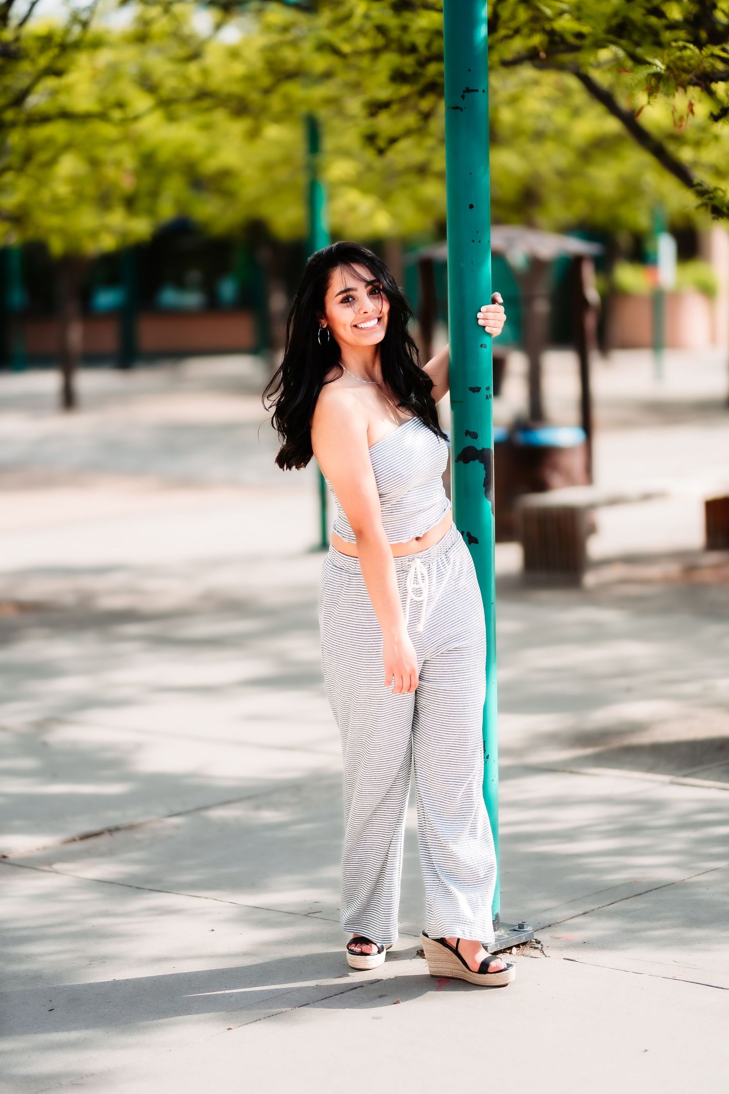 A relaxed outdoor portrait with someone leaning against a teal pole in casual grey attire.