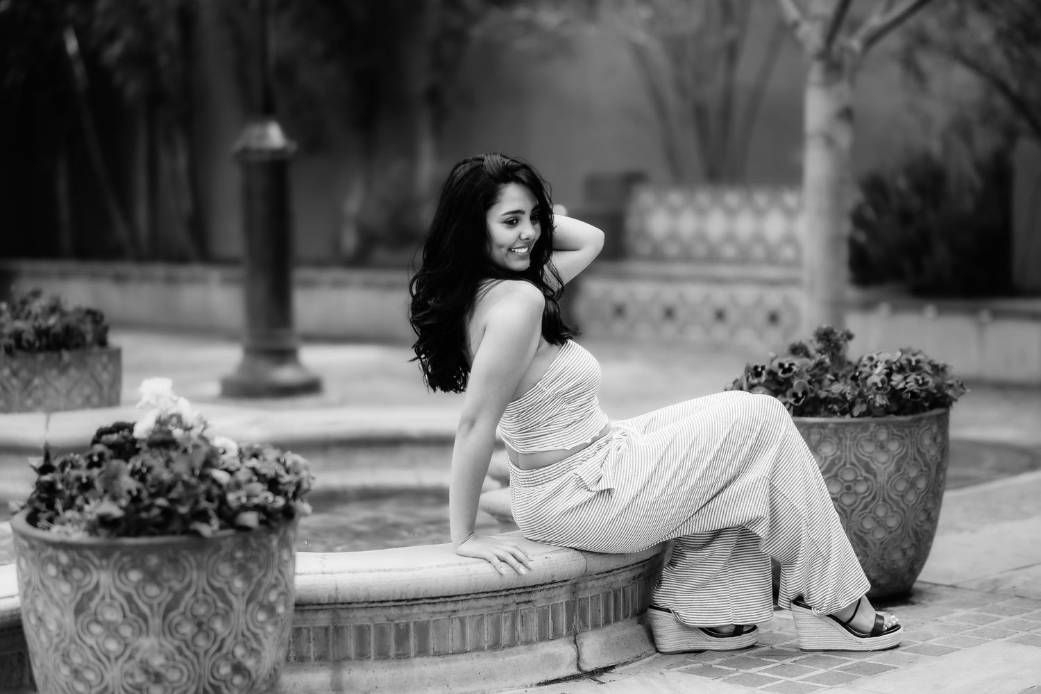 Woman in light dress reclines elegantly on stone ledge in black and white outdoor setting.