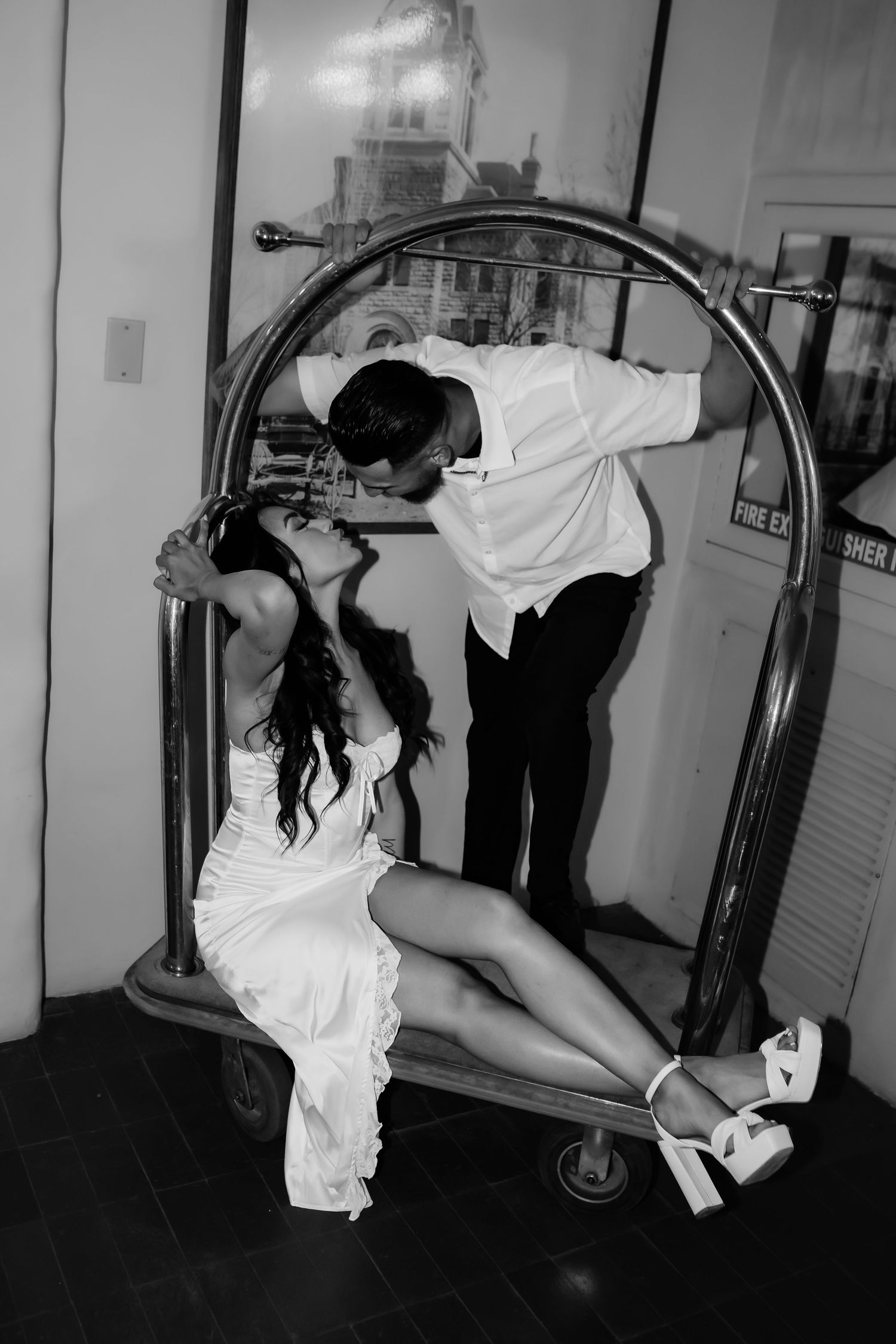 A stylized black and white photo of a couple posing on a hotel luggage cart.