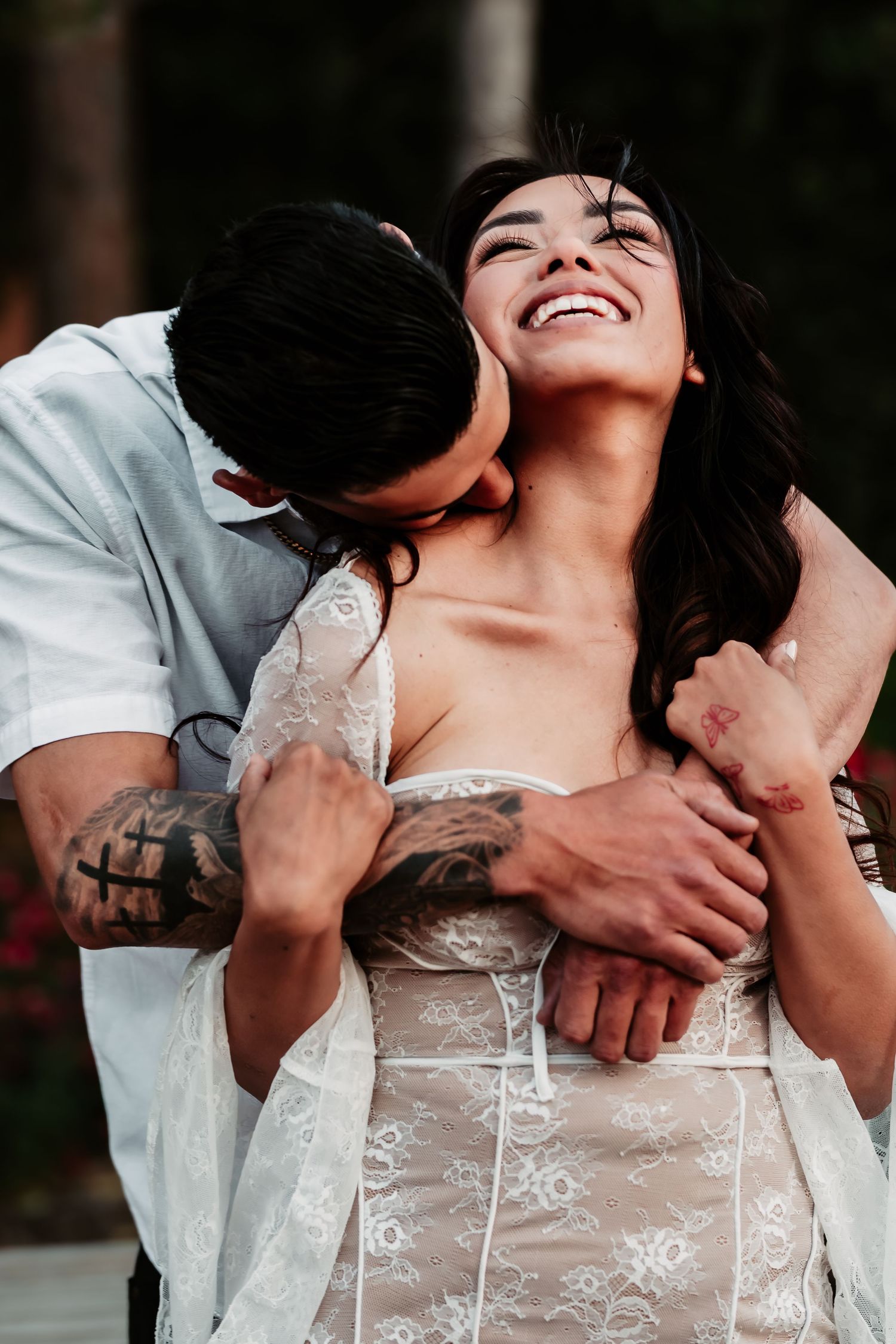 Couple sharing intimate laughing moment outdoors in white formal attire.