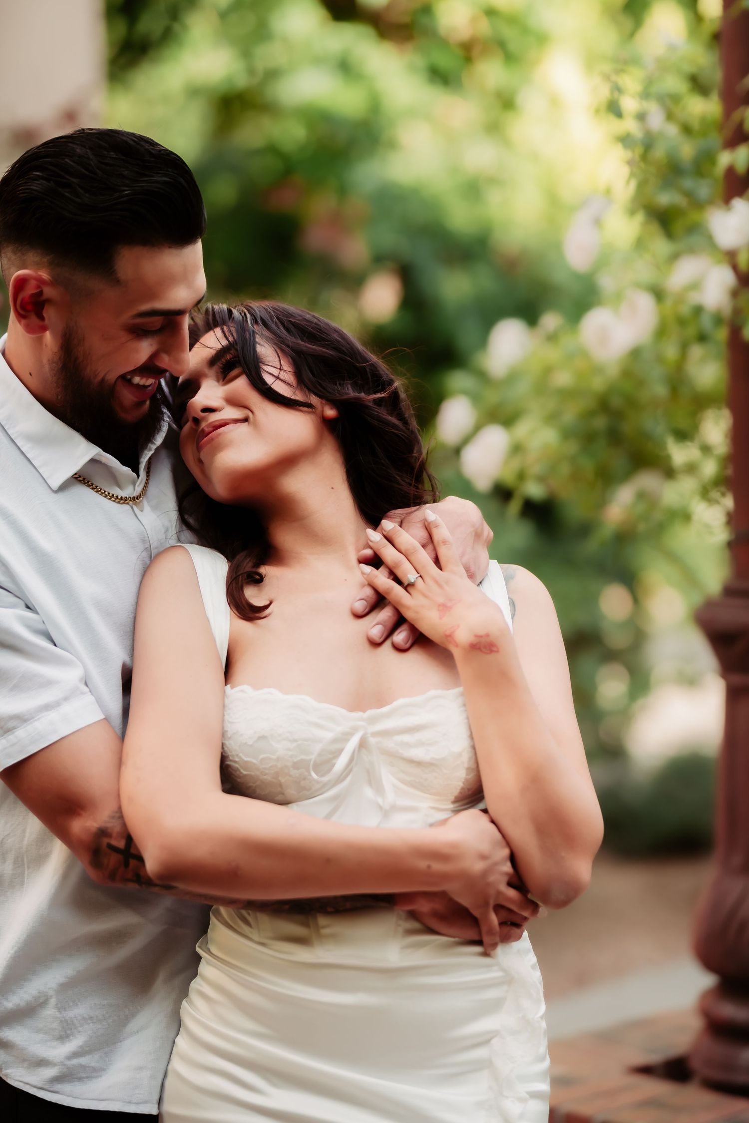 An intimate moment between a couple as they embrace and smile in a garden setting.