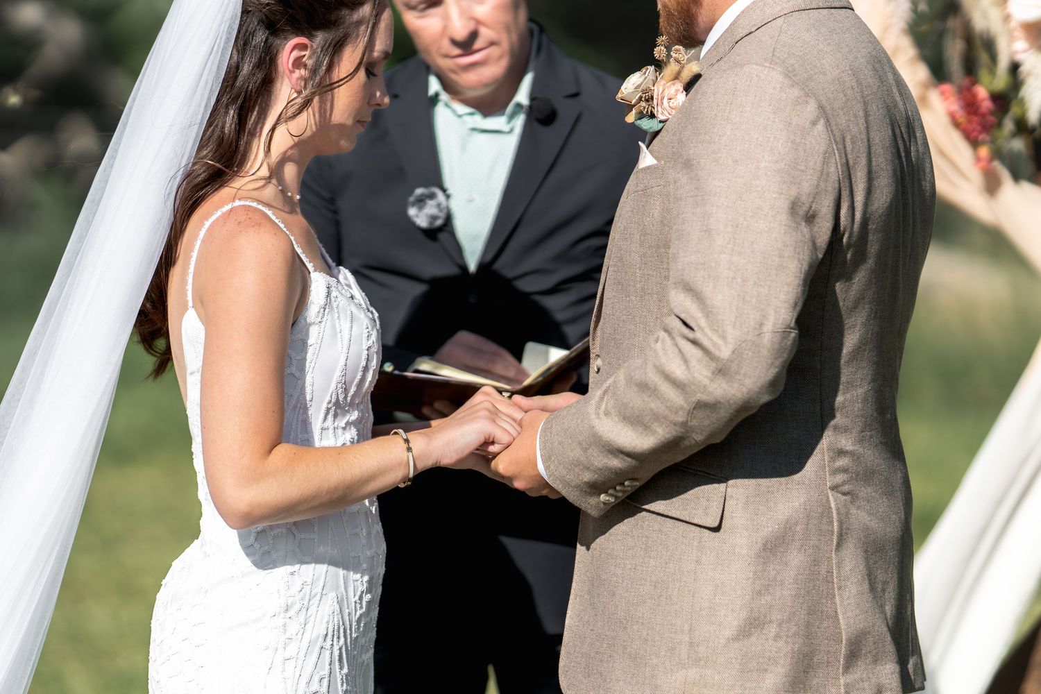 Wedding ceremony under white arch with officiant as bride and groom exchange rings.