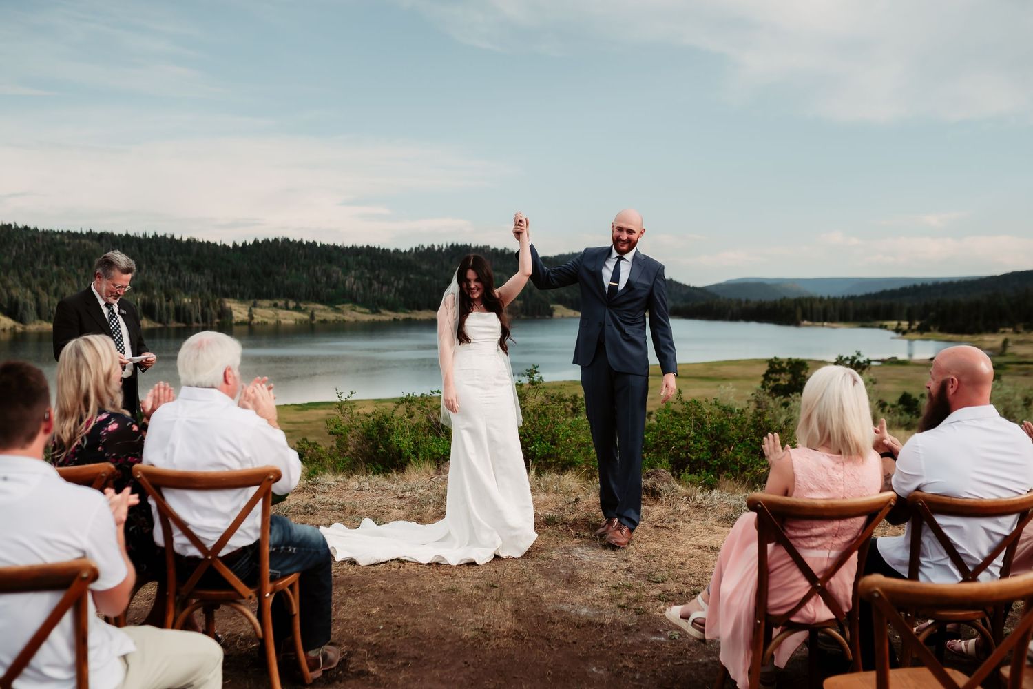 A couple celebrates during their outdoor wedding ceremony overlooking a scenic lake and mountains.
