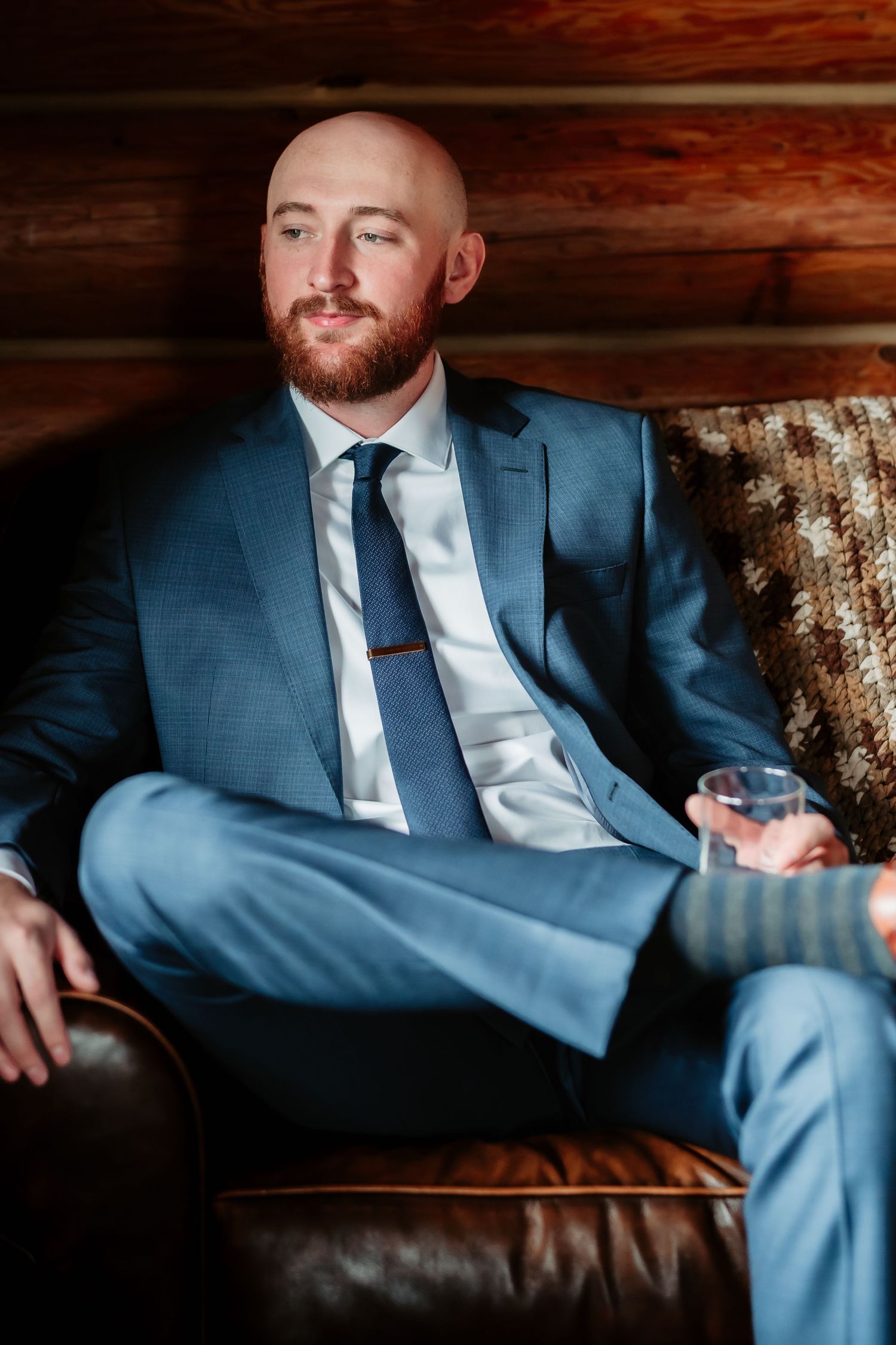 Person in blue suit relaxing on leather sofa in dimly lit rustic cabin setting.