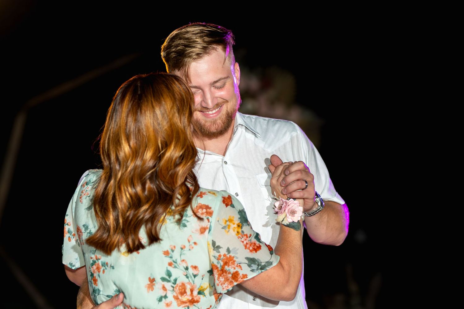 A couple shares an intimate dance moment under colorful reception lighting.