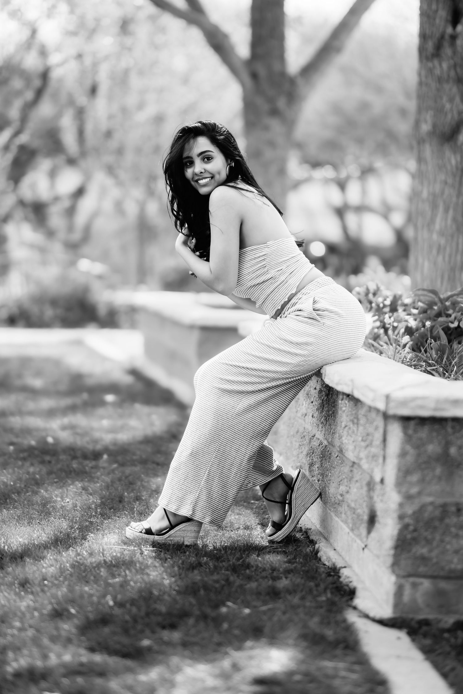 Black and white photo of a woman in casual attire leaning against an outdoor stone wall.