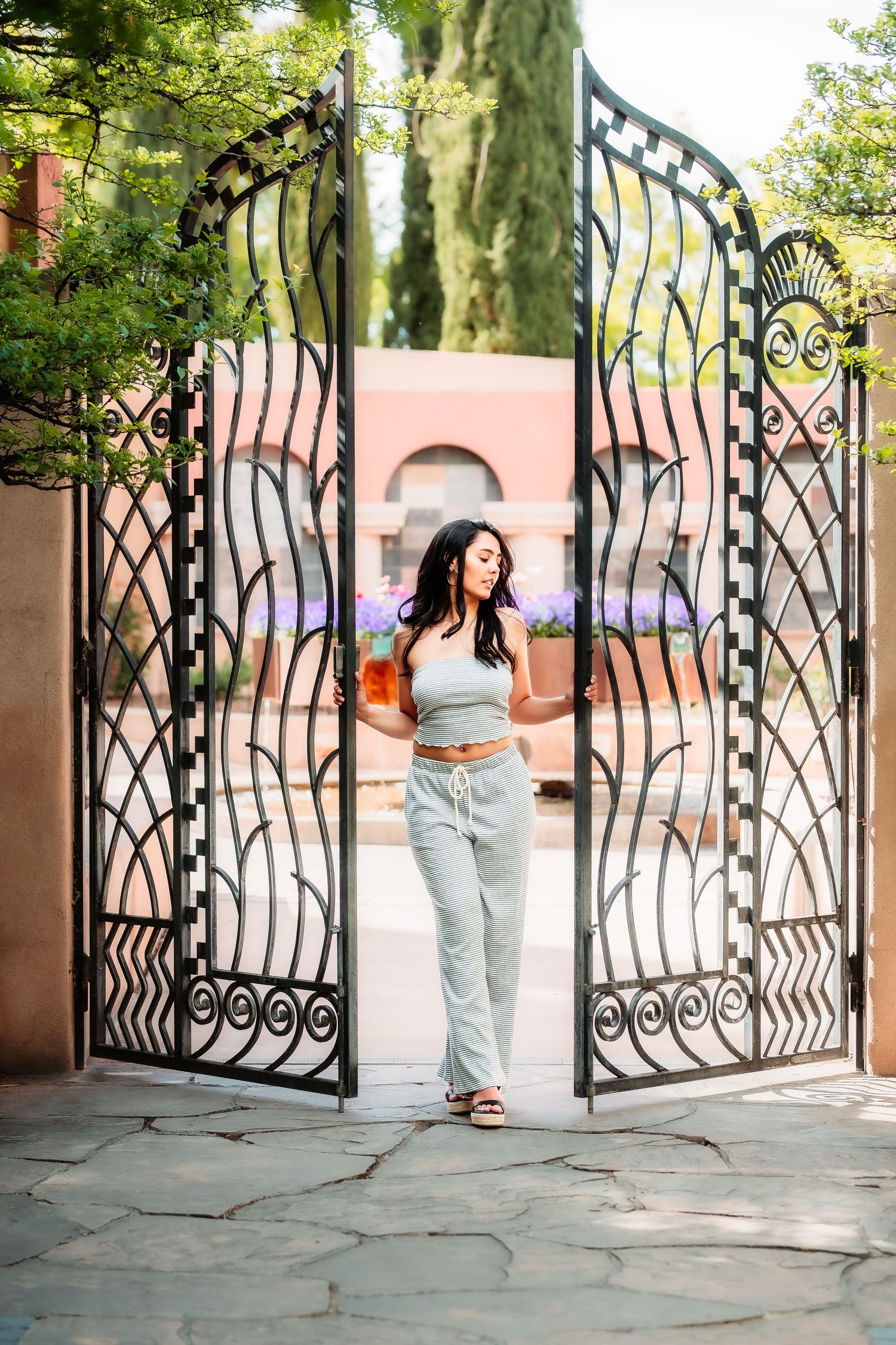 Casual pose in front of ornate wrought iron gates with decorative patterns.