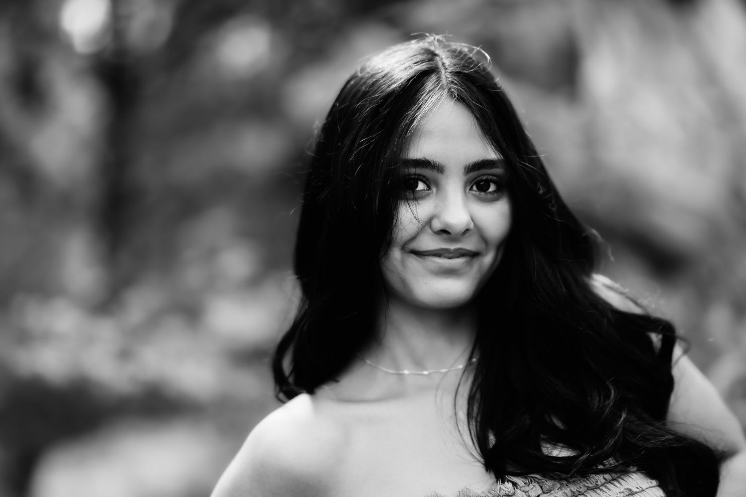 Black and white portrait of a woman with long dark hair smiling against a blurred natural background.