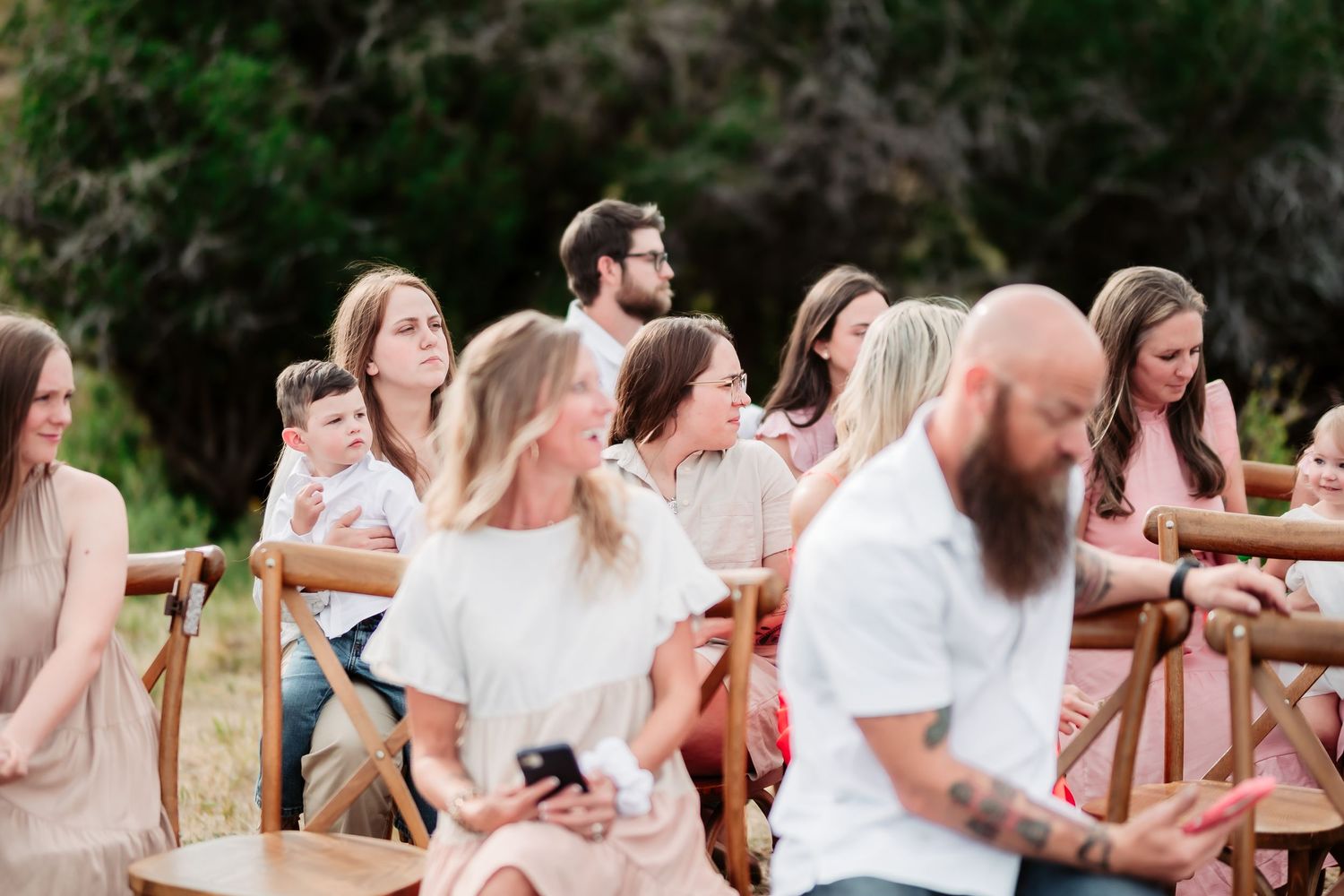 Wedding guests laugh and celebrate together at an outdoor reception with rustic wooden decor.
