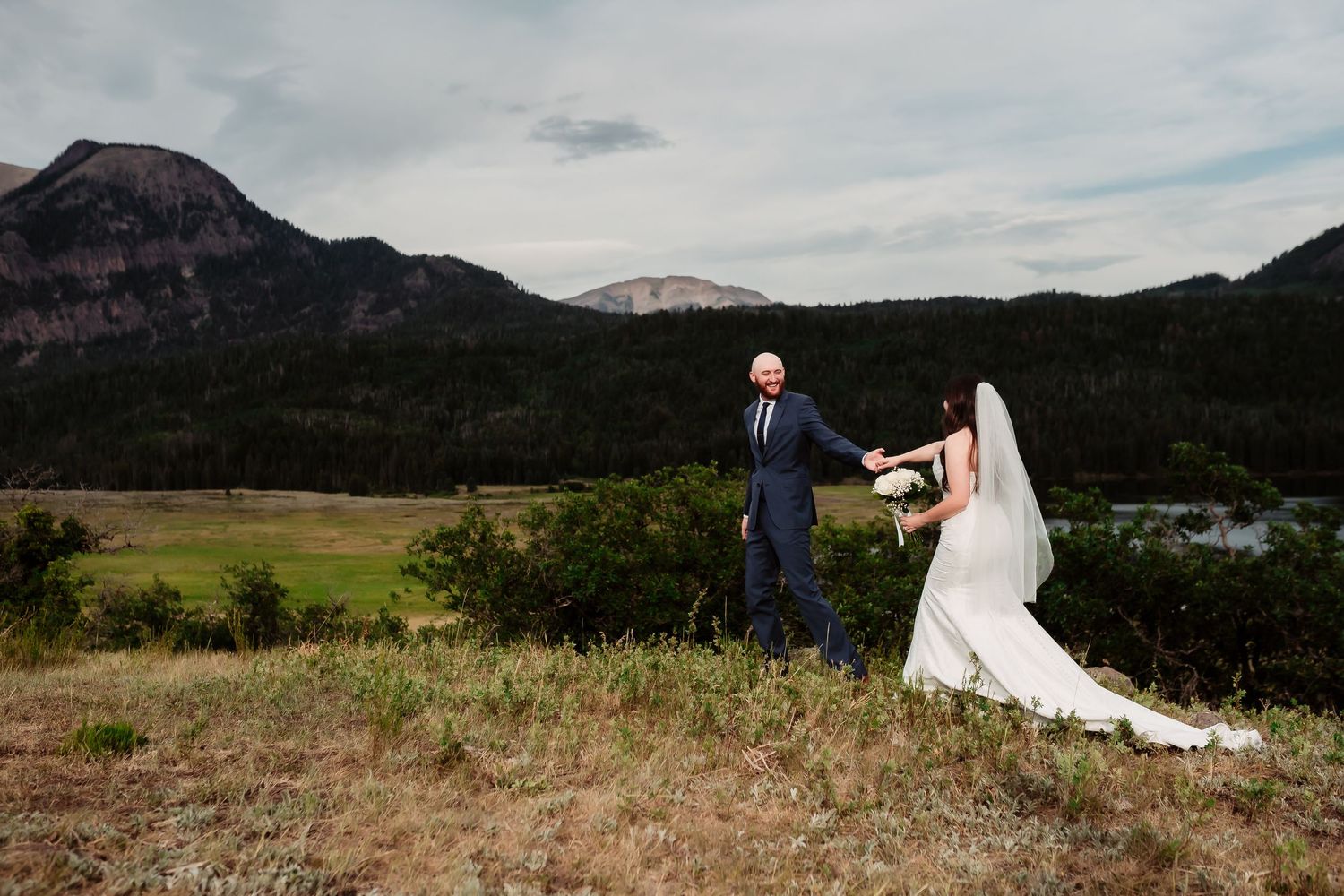 A couple in wedding attire dances together against a mountain backdrop on their wedding day.