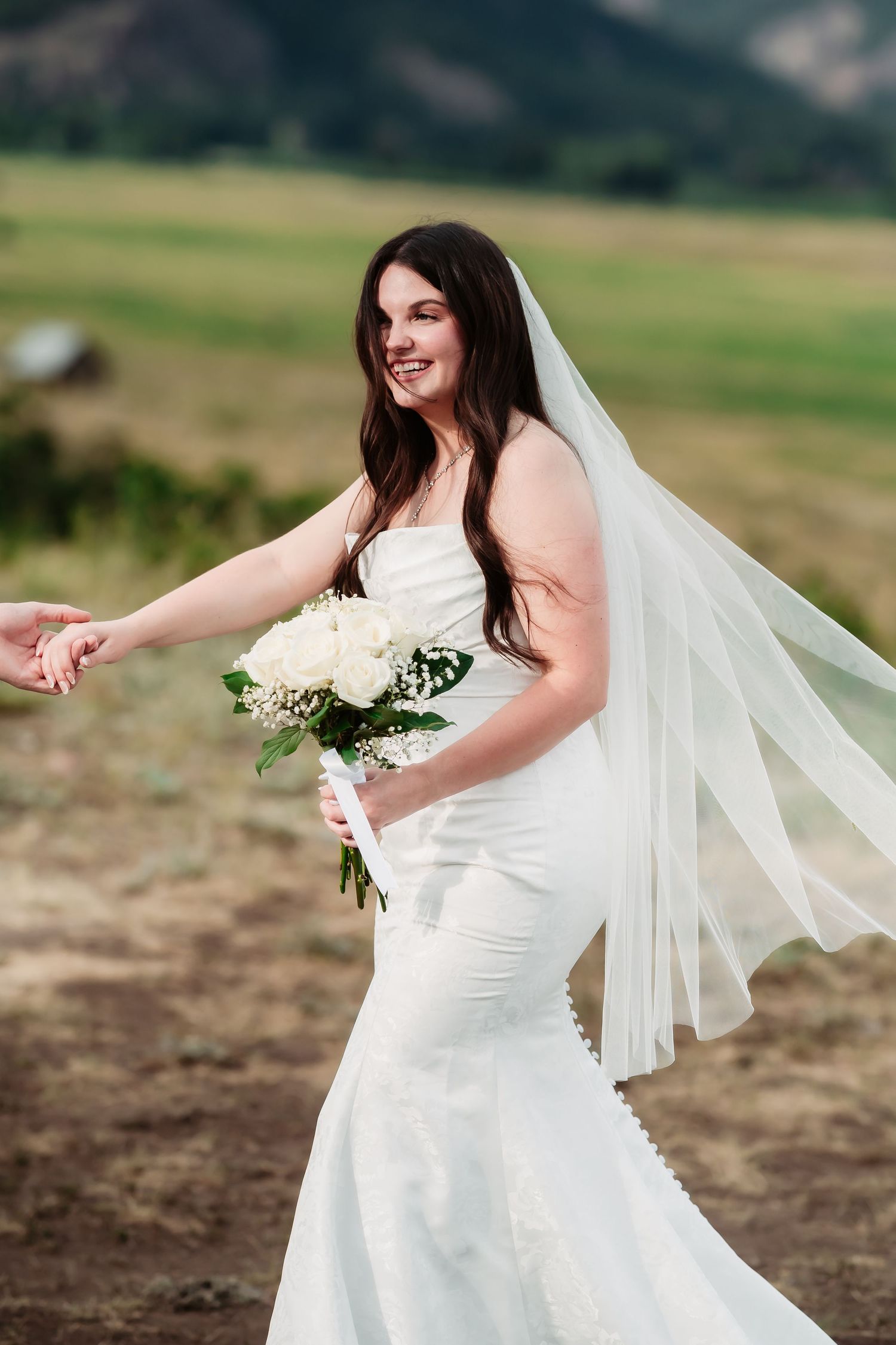 Bride in white dress holding bouquet poses against mountain backdrop.