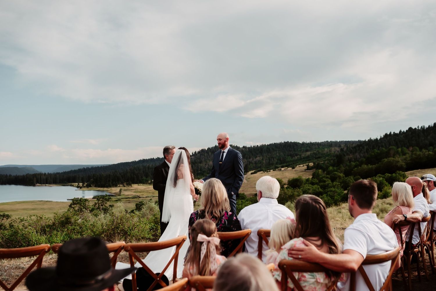 Wide panoramic view of mountain wedding ceremony with guests and natural scenery.