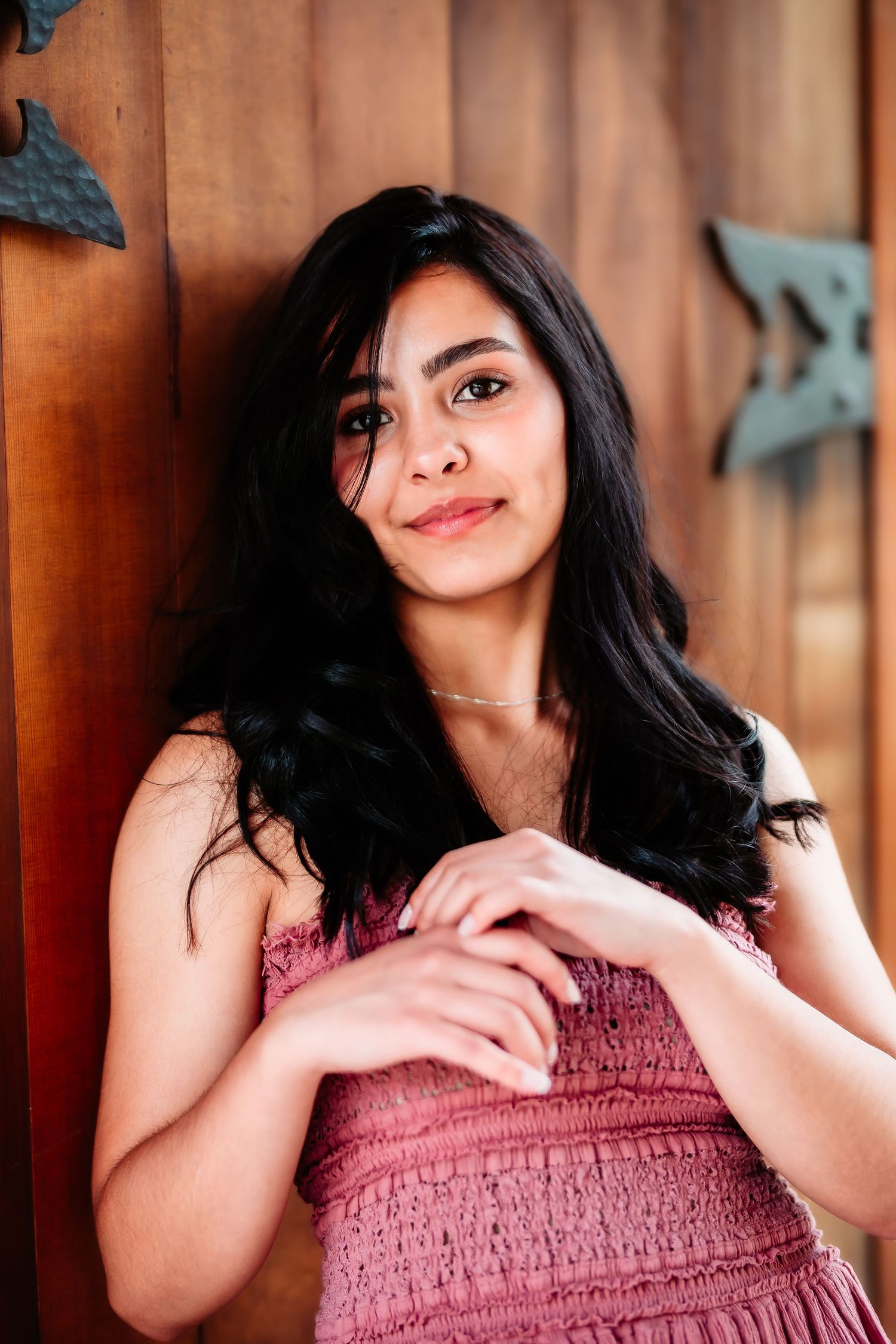 Smiling woman in pink shirred dress posing against wooden wall with decorative butterflies.