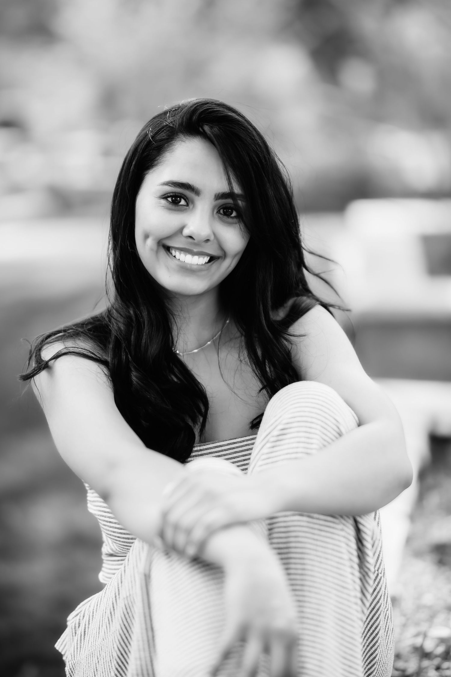 A black and white portrait of someone in a striped top sitting outdoors with a natural smile.