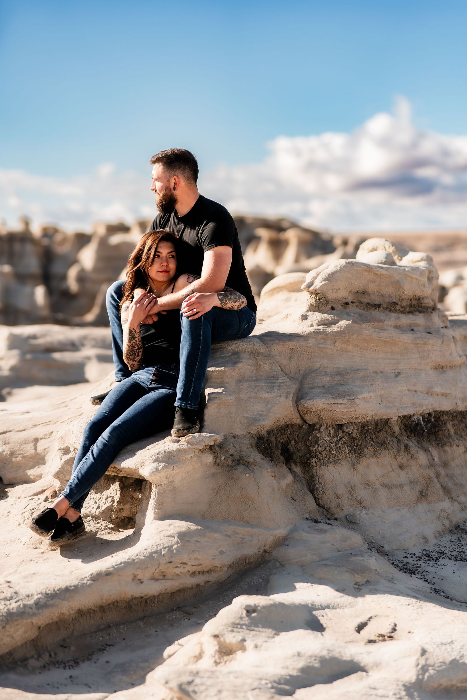 Couple sitting together on white rock formations under blue sky with puffy clouds during a sunny day.