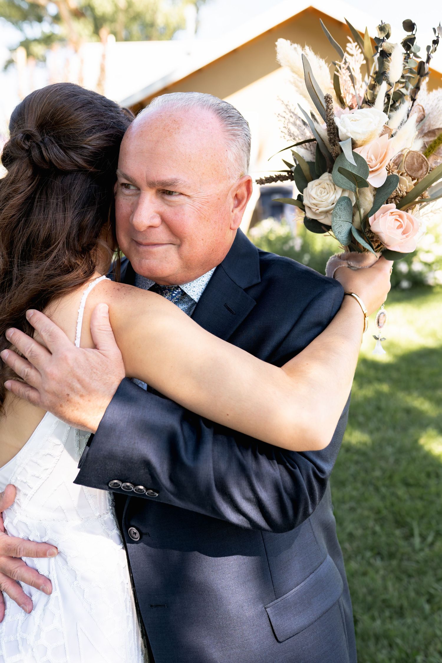 Emotional wedding moment as couple embraces outdoors with a beautiful white and blush floral bouquet.