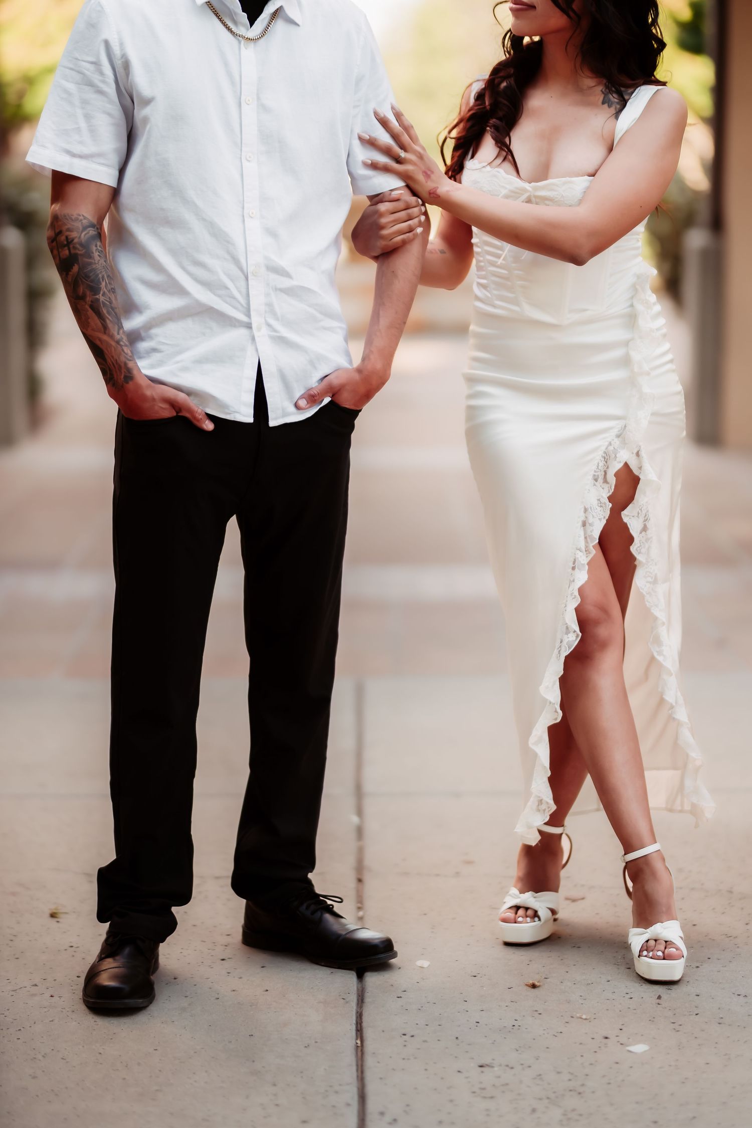 Modern wedding photo featuring contrast of casual groom in white shirt and dark pants with bride in elegant slit dress.