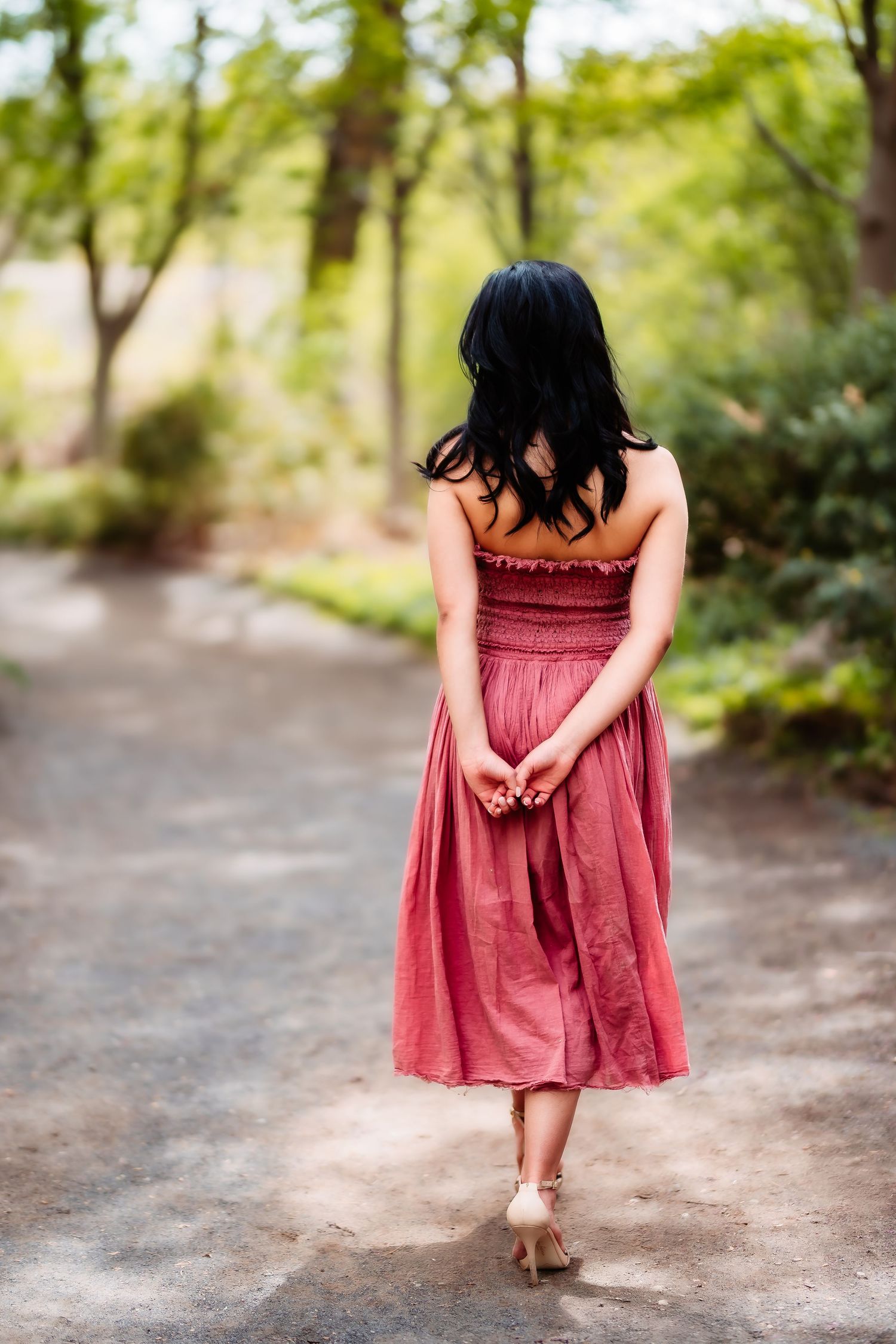 Back view of someone walking down a nature path wearing a red midi dress and heels.