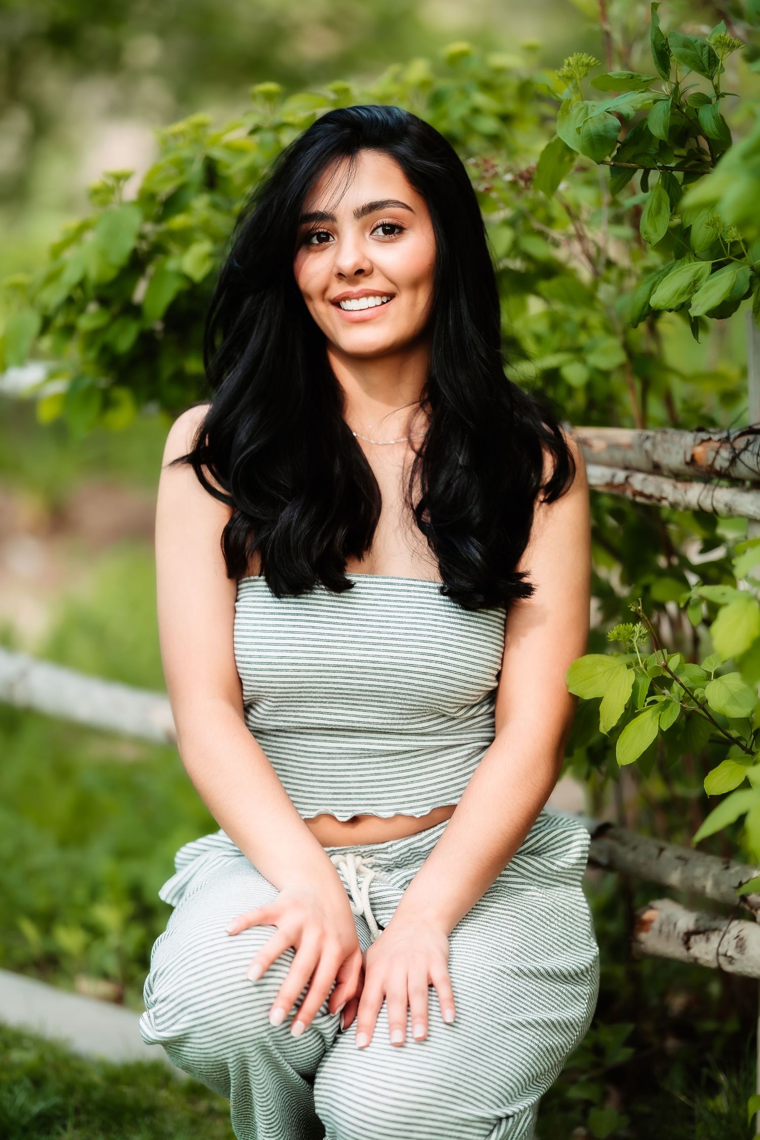 A woman in a striped crop top sits among green foliage on a summer day.