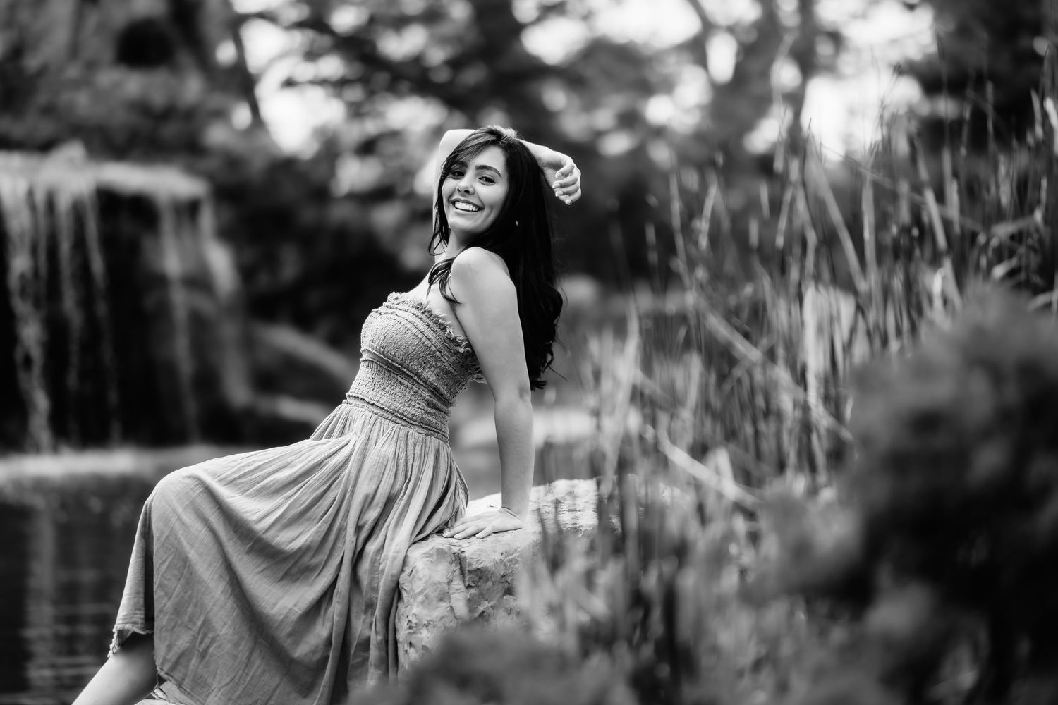 Monochrome photo of a person in a long dress posing gracefully near water and tall grass.