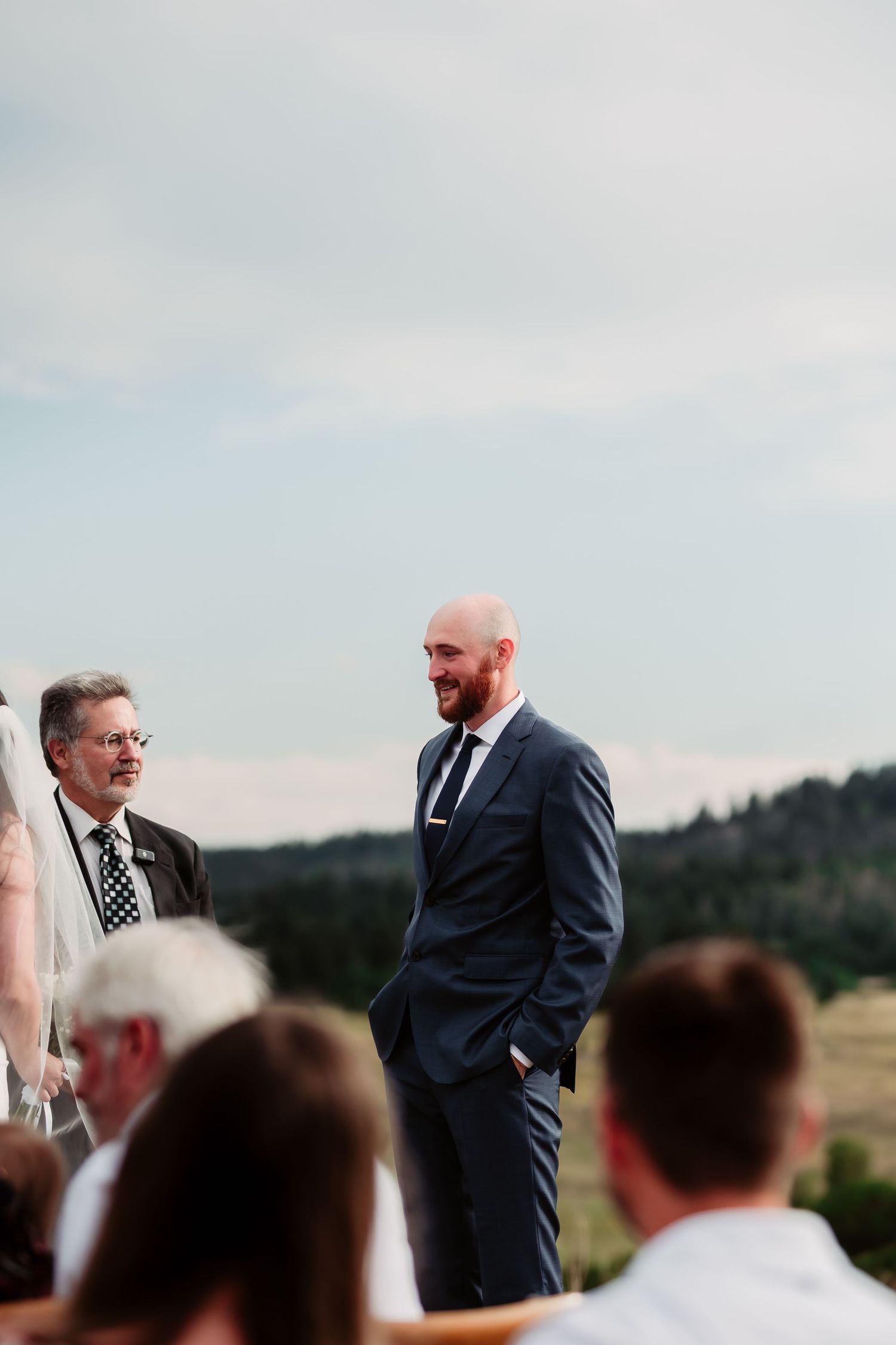 Intimate outdoor wedding ceremony with mountain backdrop and guests seated on rustic chairs.