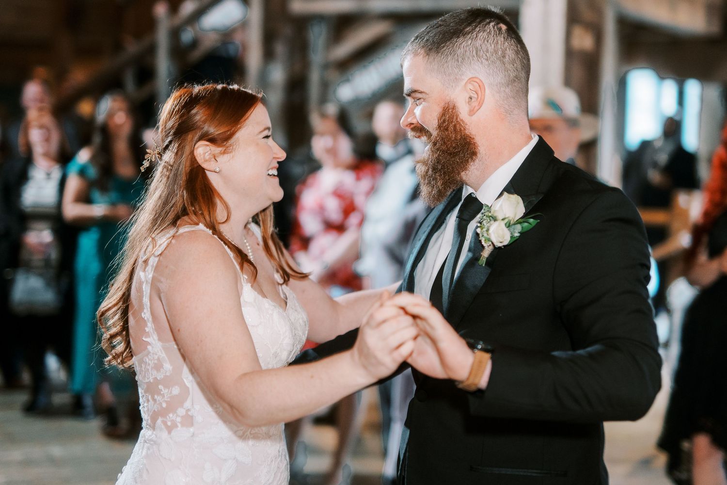 A couple shares their first dance at a rustic indoor wedding venue with soft natural lighting.