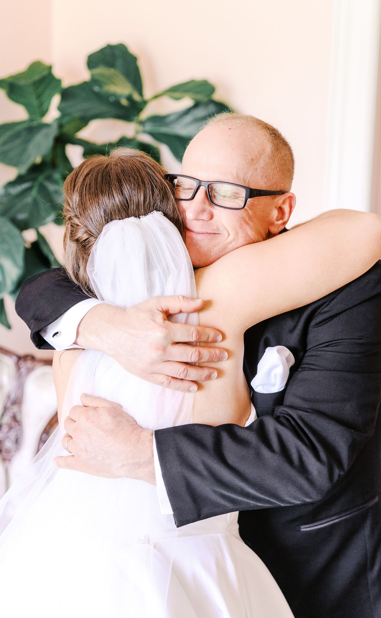 An emotional embrace during a wedding celebration with indoor greenery in the background.