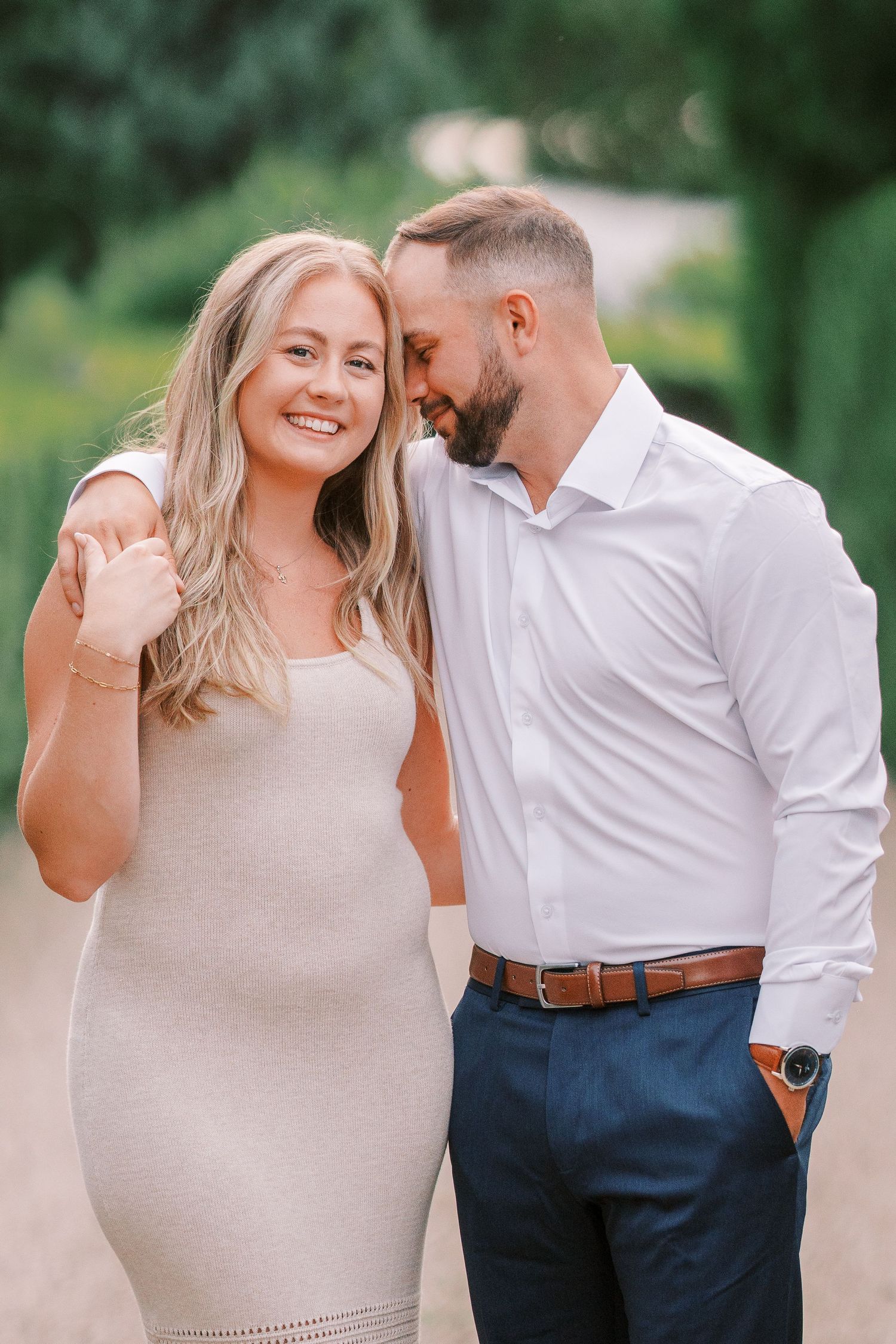 Engaged couple embraces in a romantic outdoor photo session wearing beige sweater and white shirt.