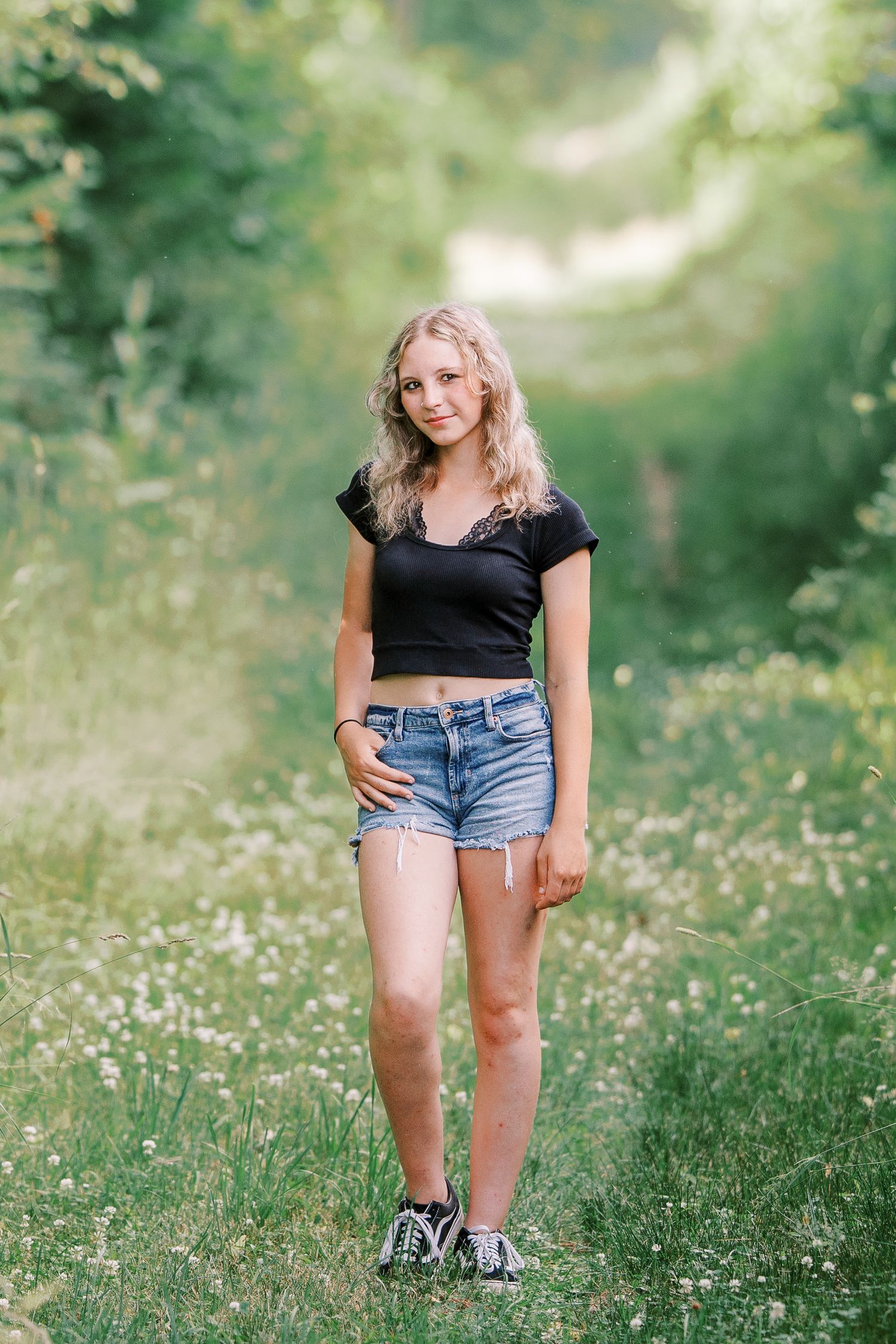 A person in jean shorts picks wildflowers in a lush green field on a summer day.
