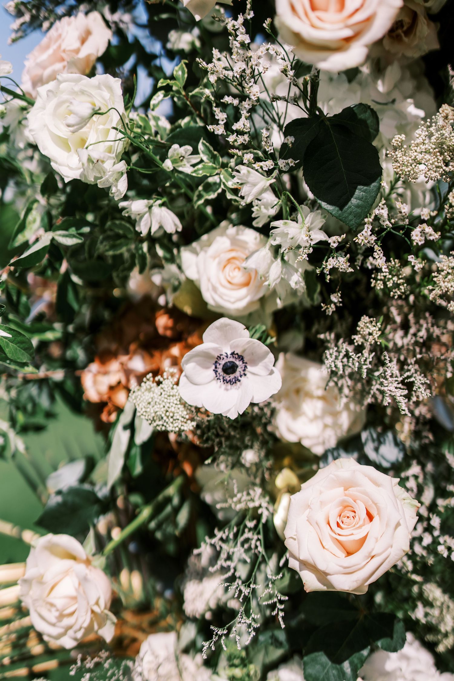 Close-up of blush pink roses and white anemone flowers with baby's breath in a lush floral arrangement.
