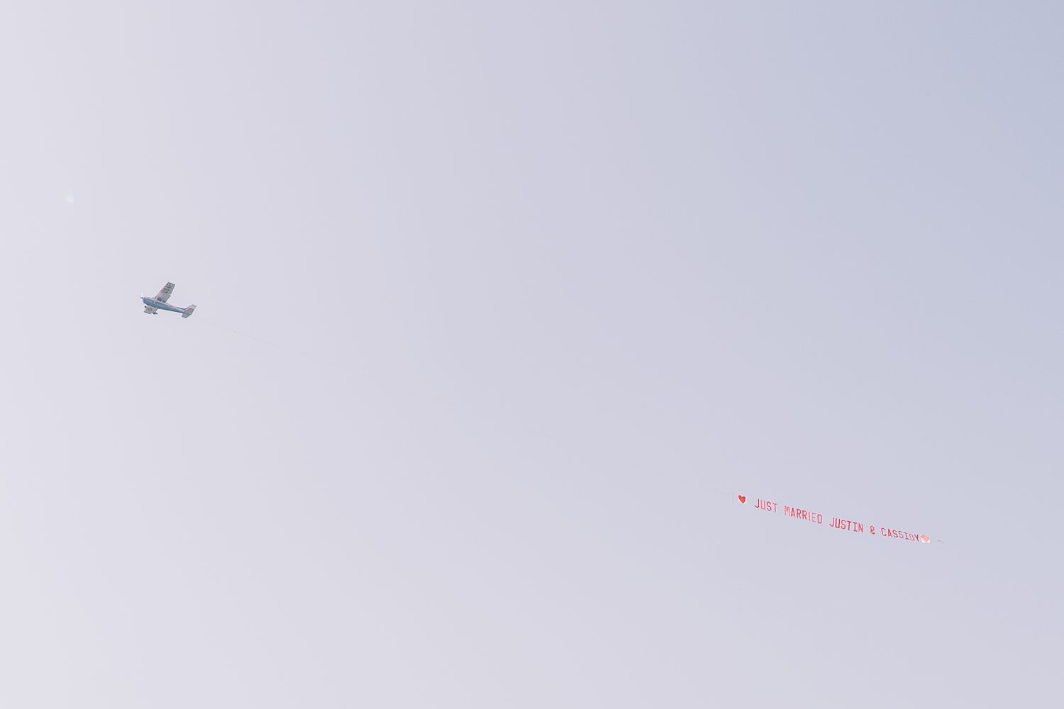 A small airplane soars through a pale gray sky with a thin red line visible in the distance.