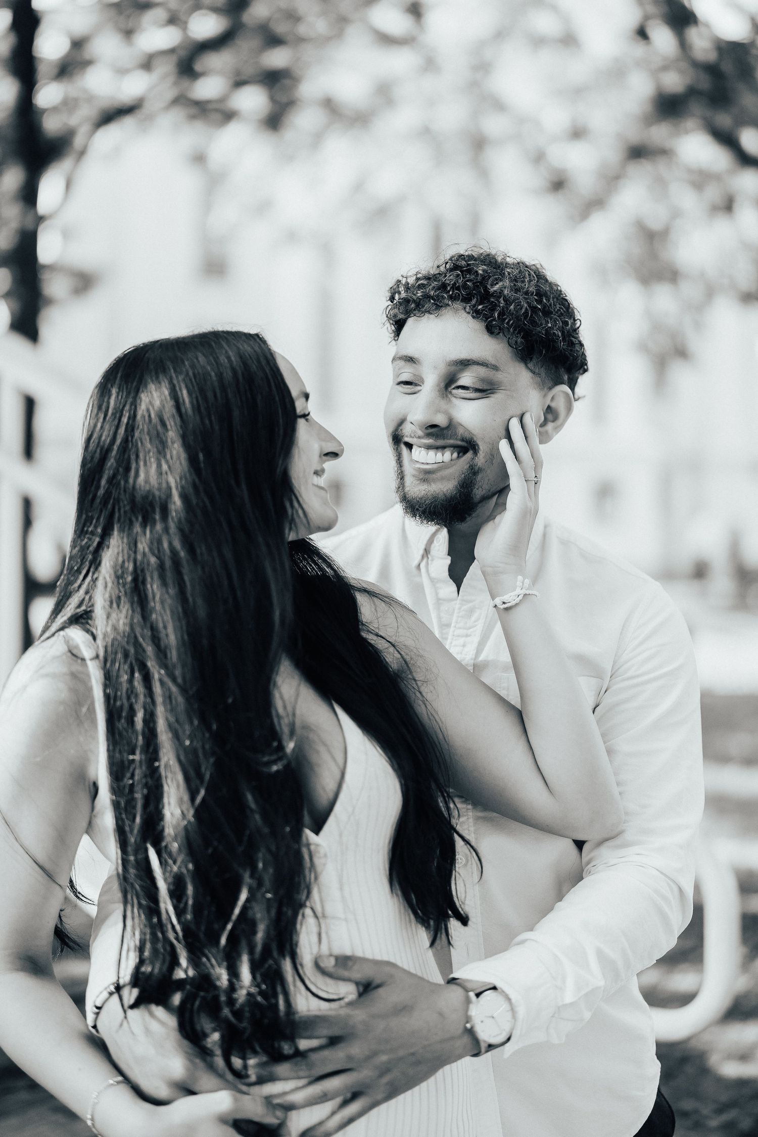 A romantic couple shares a joyful moment together outdoors in a black and white photo.