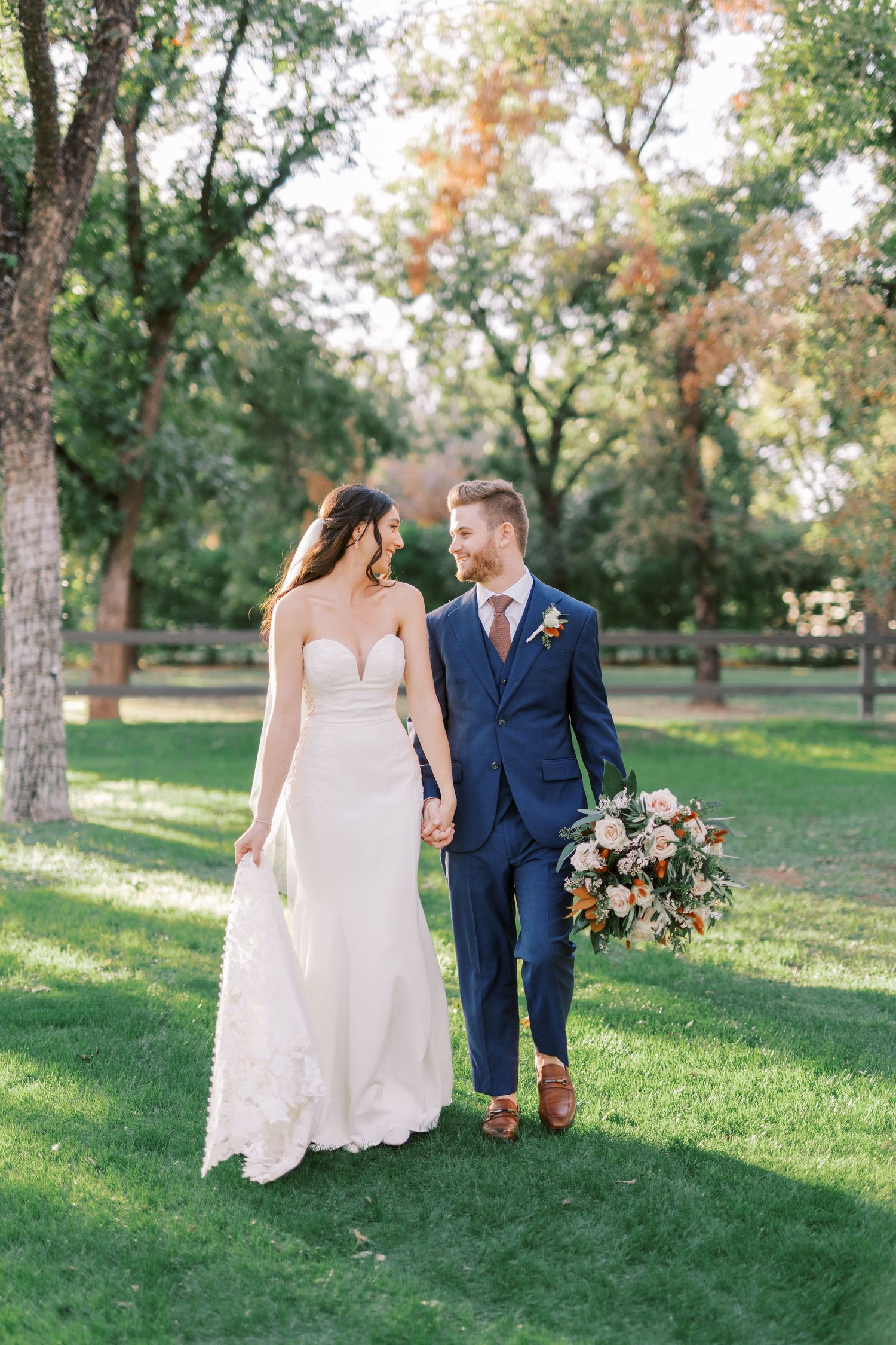 A couple in formal wedding attire walk together and share moments on a grassy hill during an autumn outdoor photo session.
