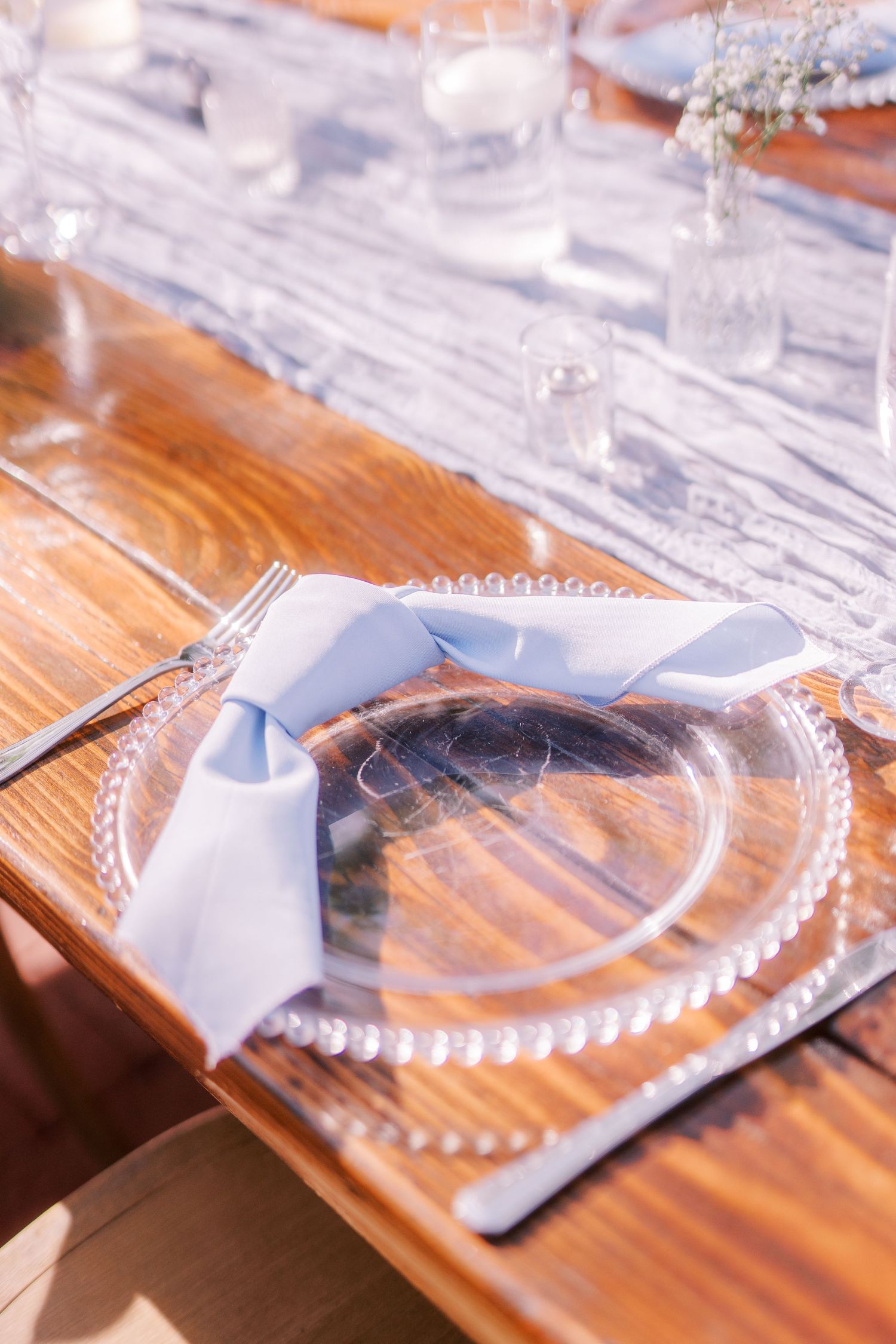 Elegant glass charger plate with light blue bow ribbon on rustic wooden table set for formal dining.