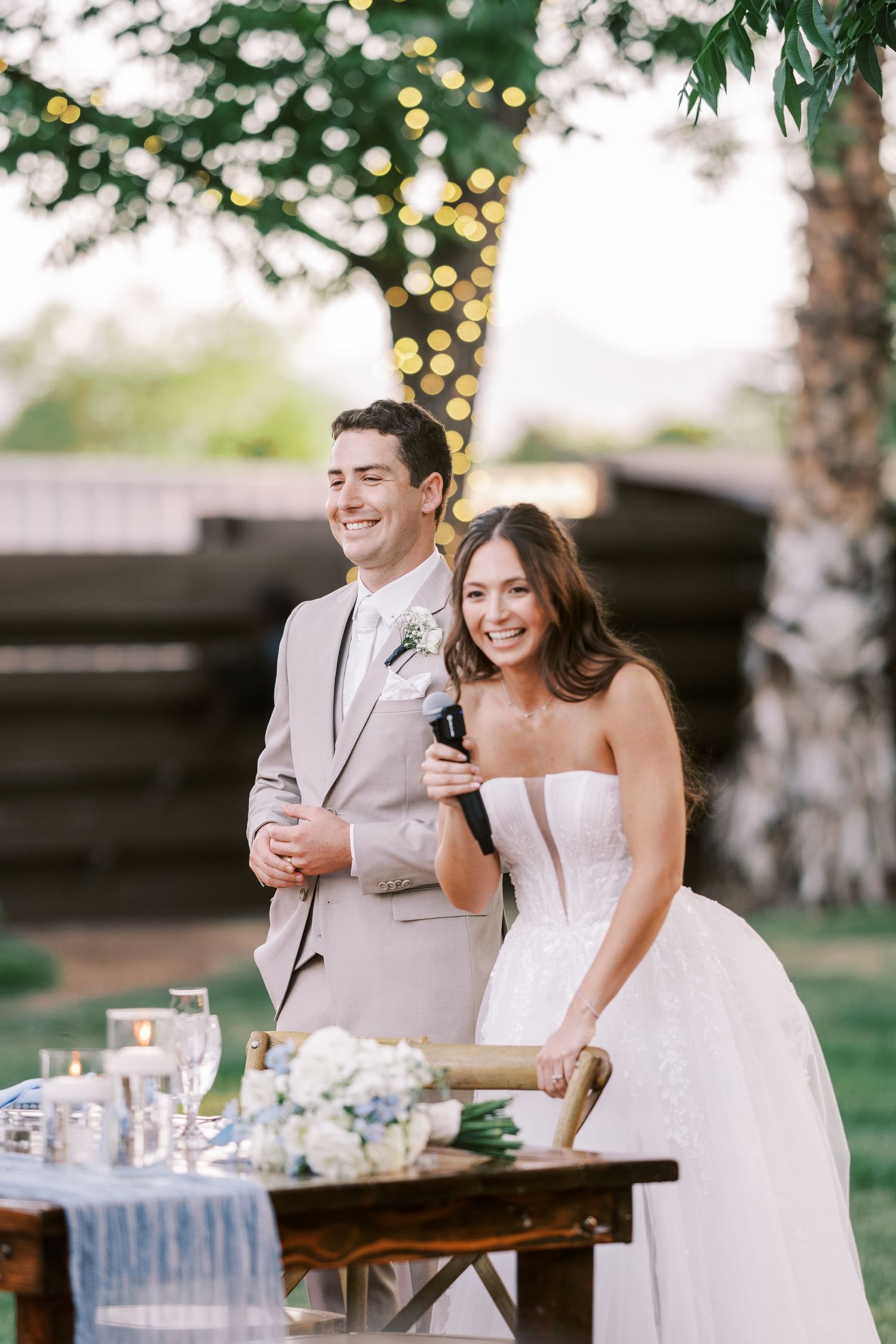 A couple shares a joyful moment together at their outdoor wedding reception with twinkling lights in the background.