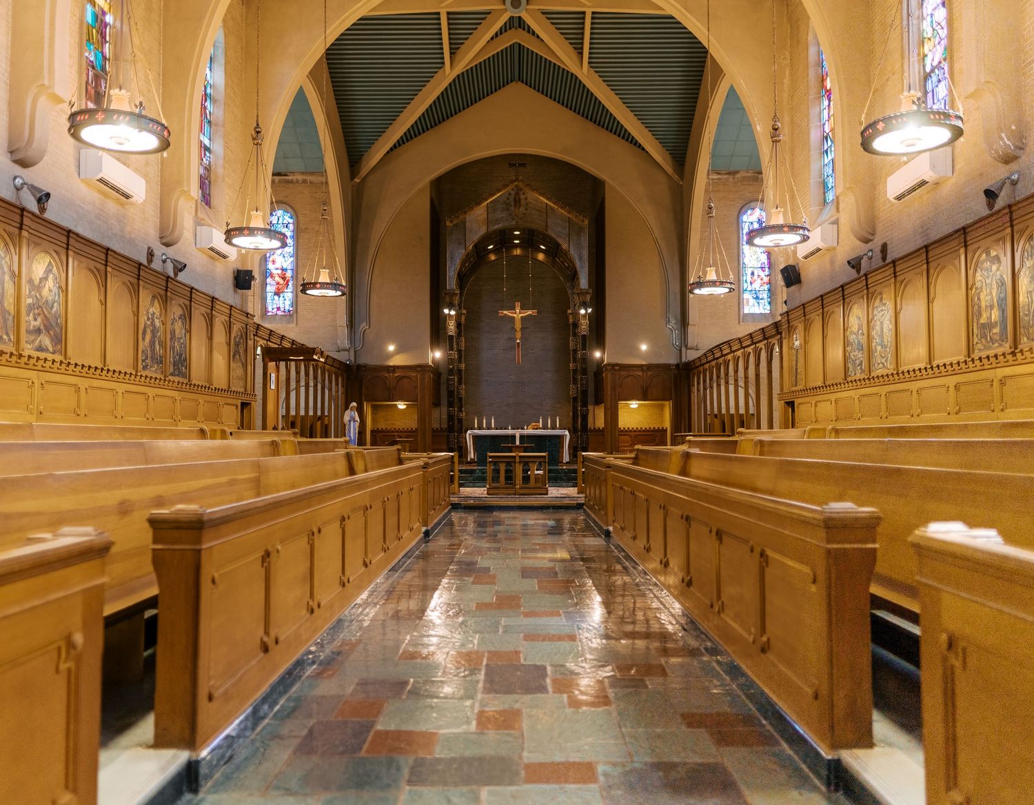 A warm-lit church interior with wooden pews and stone flooring showcases traditional Gothic architecture and elegant lighting.