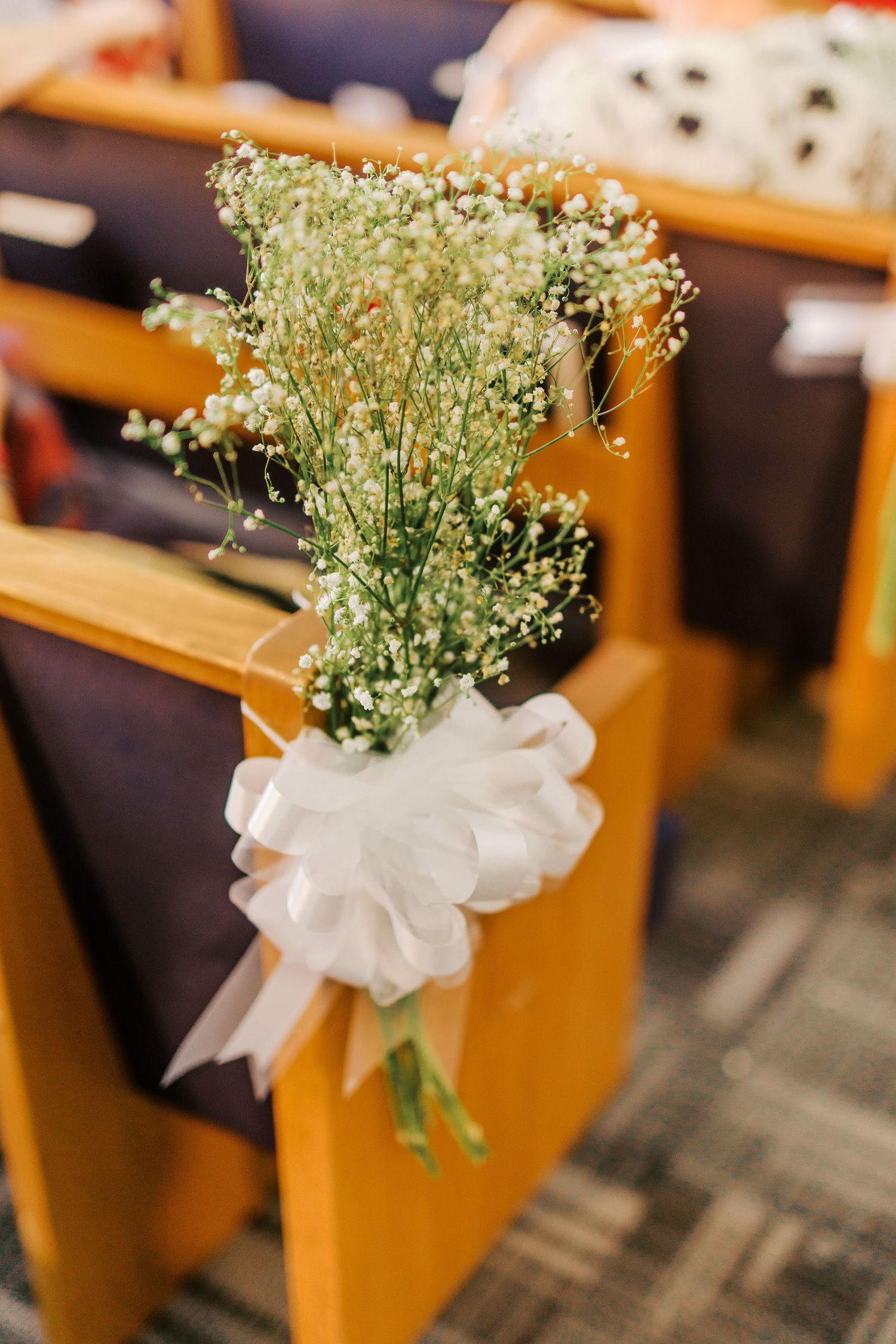 White baby's breath flowers and bow decorate a wooden church pew for a wedding ceremony.