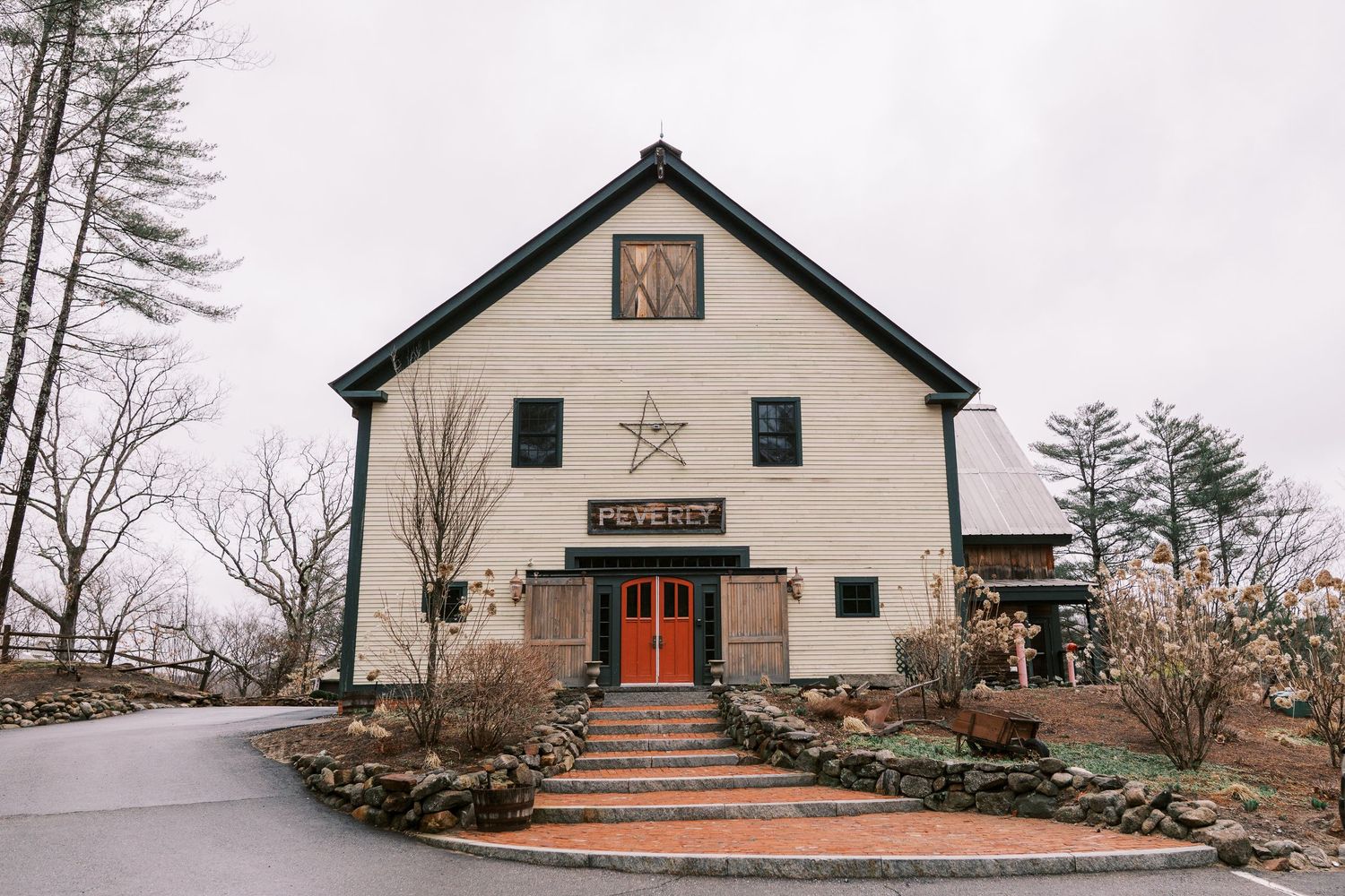 A rustic white barn-style building with a decorative star and red door, featuring stone steps and natural landscaping.
