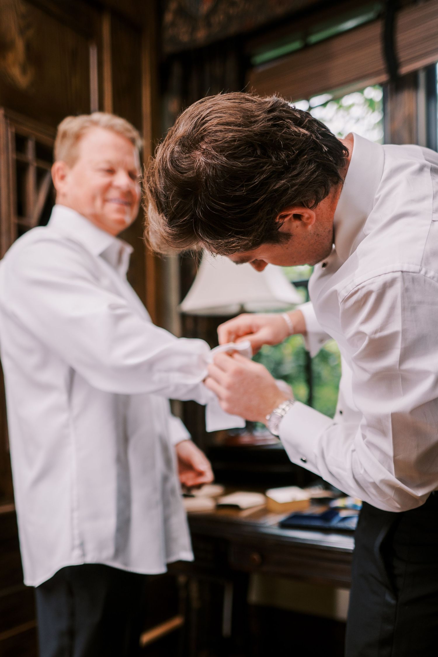 Two people in white shirts helping each other get dressed for a formal occasion.