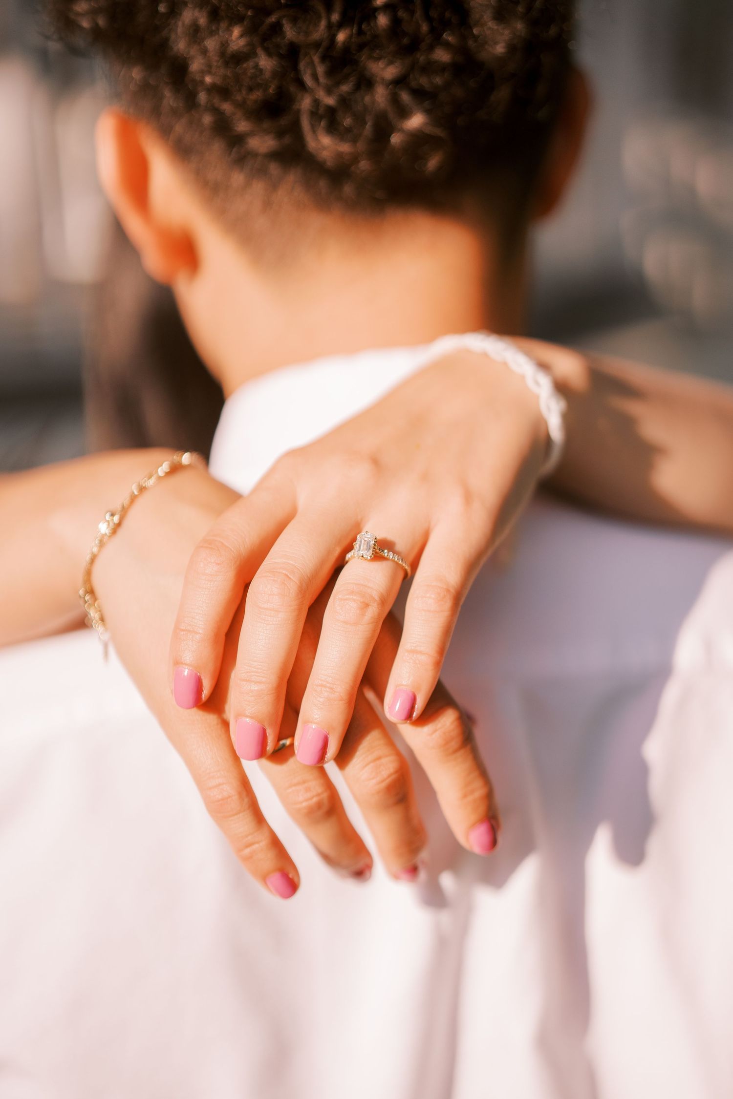 Close-up of hands with an engagement ring and delicate bracelet in warm sunlight.