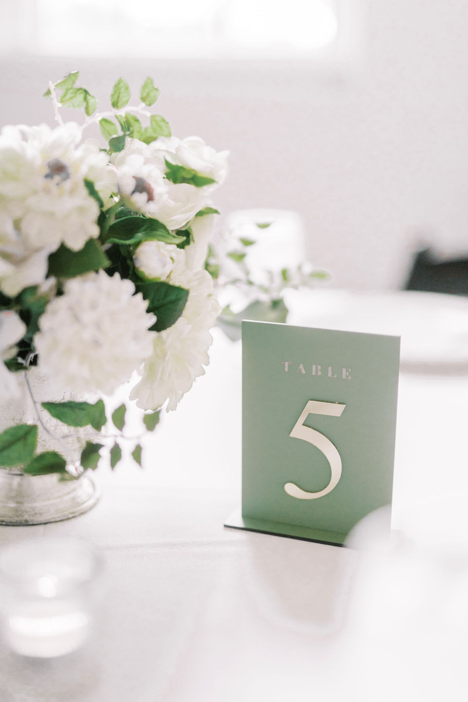 Minimalist sage green table number five card with white floral centerpiece.