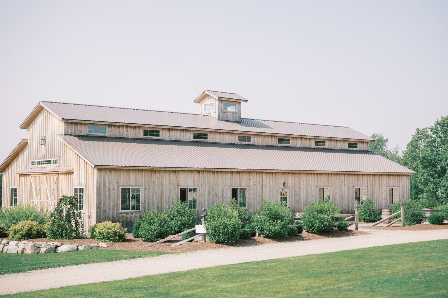 A modern tan and beige barn wedding venue with lush landscaping and manicured lawns in a rustic country setting.