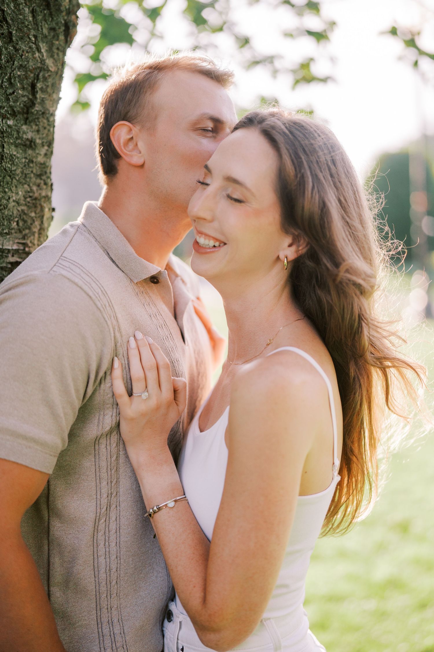 A romantic moment captured in nature as sunlight filters through trees while a couple shares an intimate embrace.